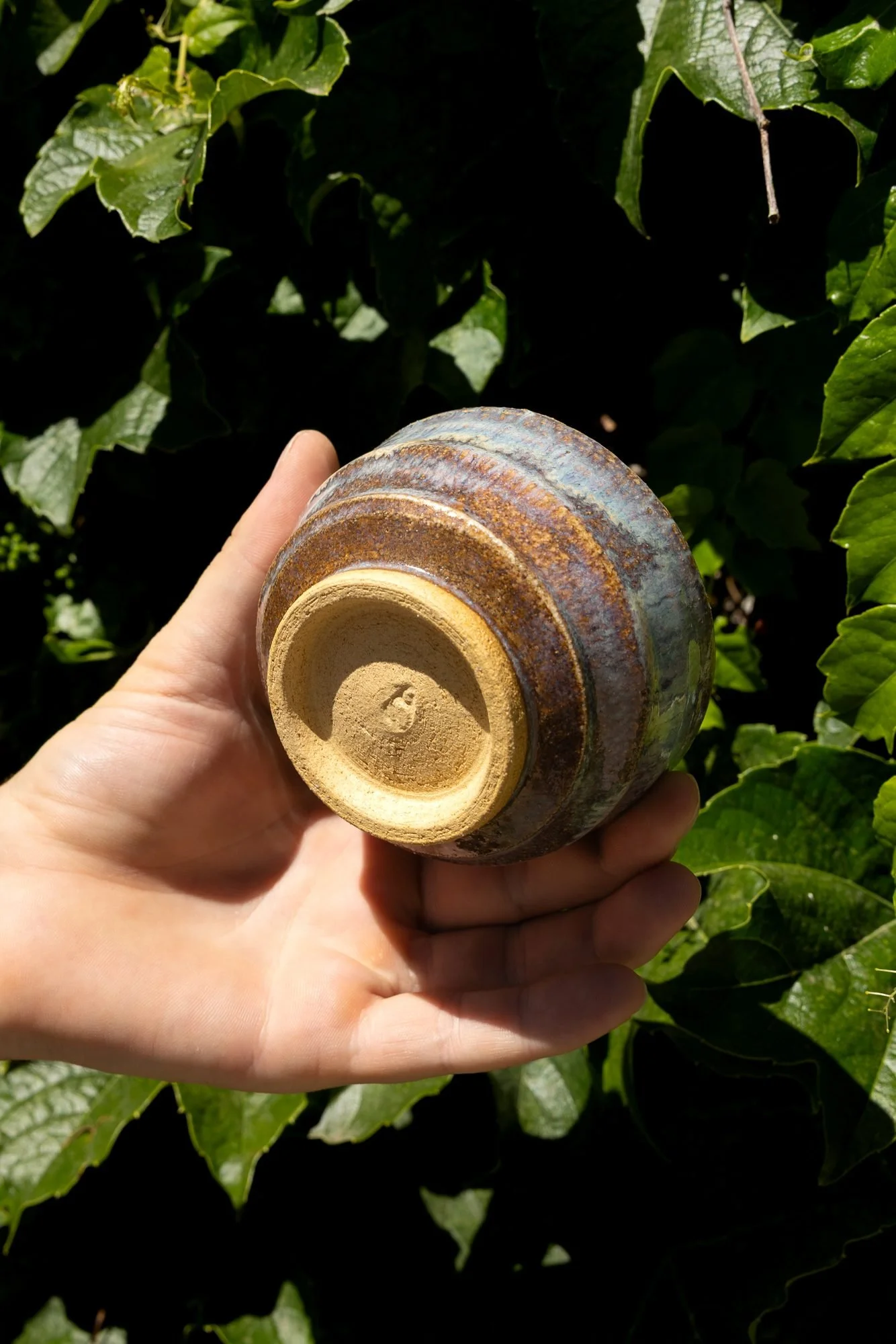 Hand holding a finished blue glazed bowl upside down showing an unglazed pale foot ring