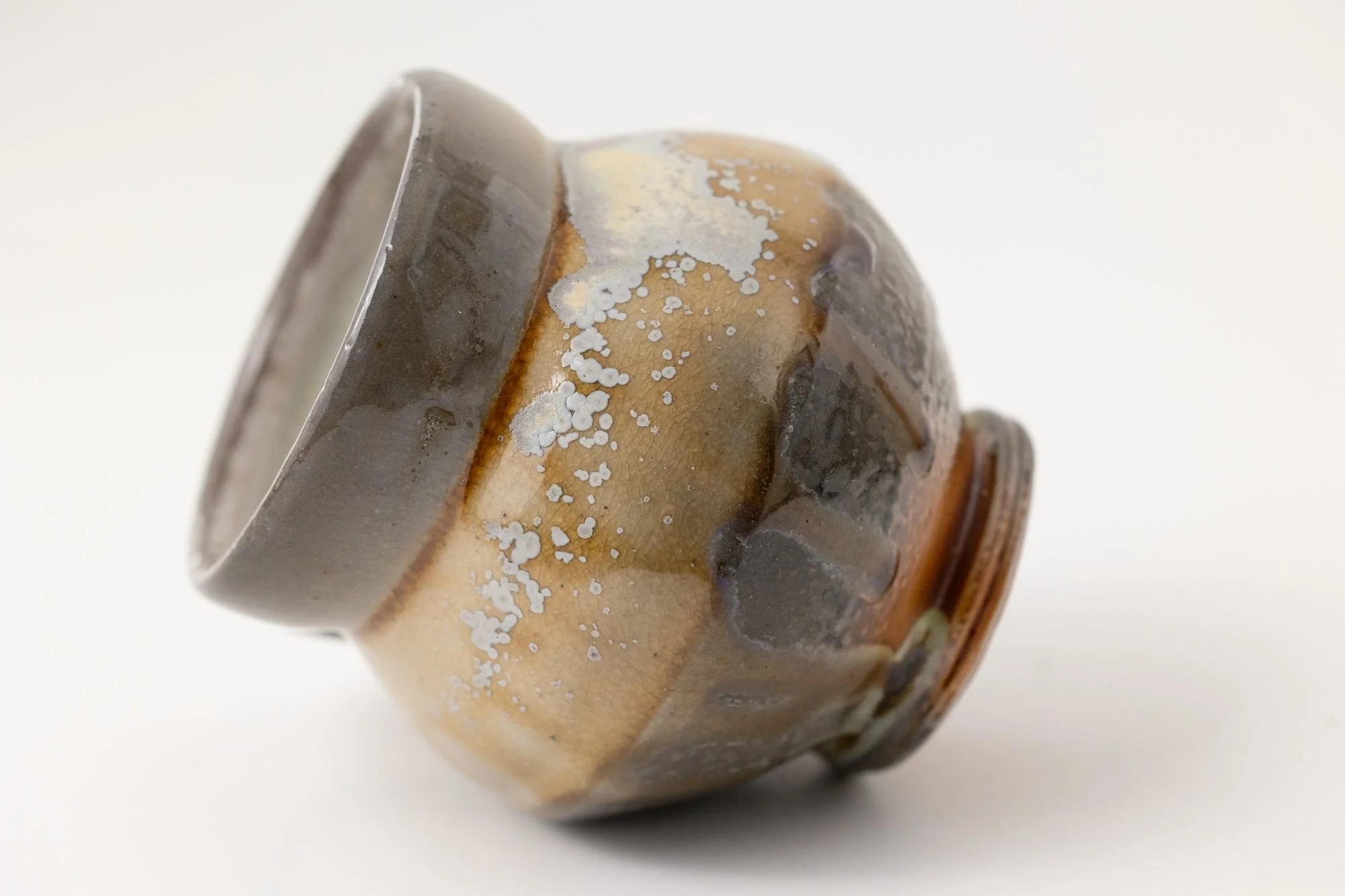 A salt-fired cup lying on its side, showing a gray rim and an amber and white flashed body