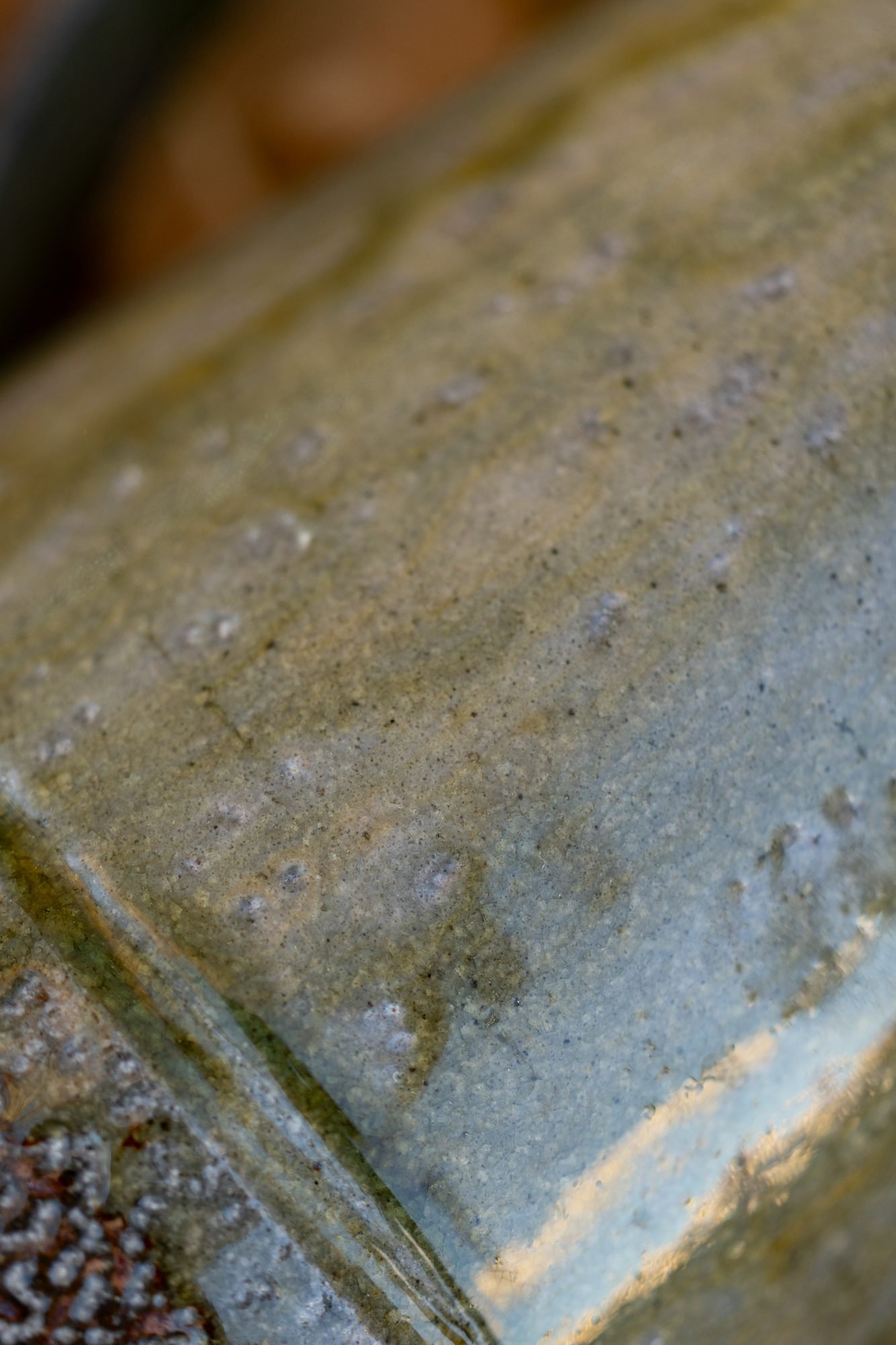Extreme close-up of a salt-fired pot showing glossy gray green glaze and a pitted orange peel surface