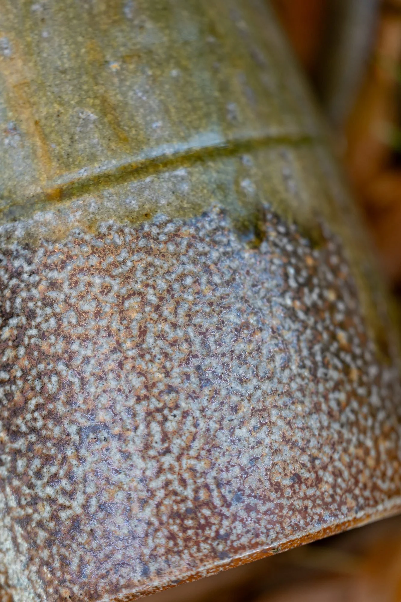 Close view of the lower half of a salt-fired pot where a glaze band meets speckled salted clay