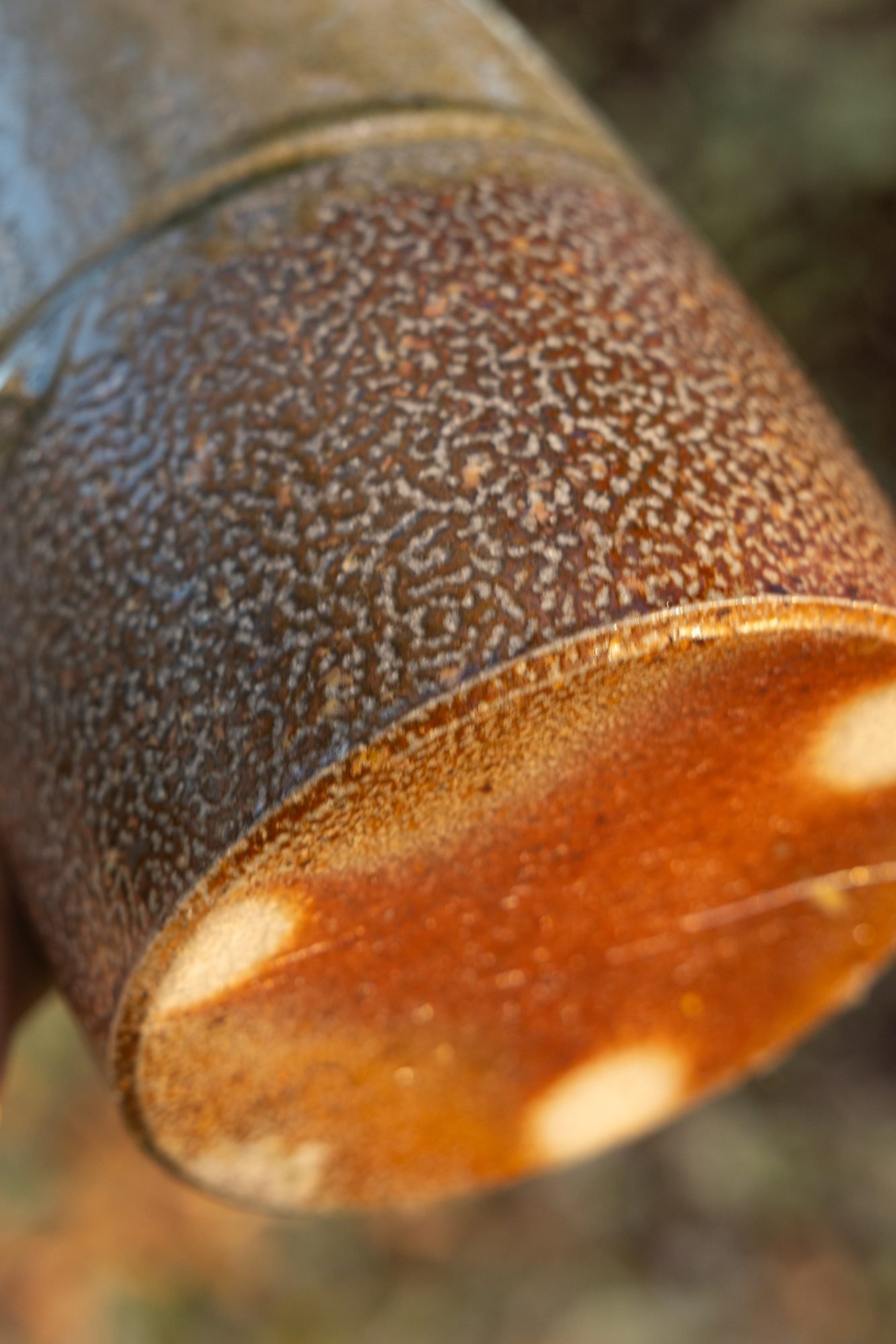Underside of a salt-fired pot held up outdoors, the foot orange with pale round wadding marks