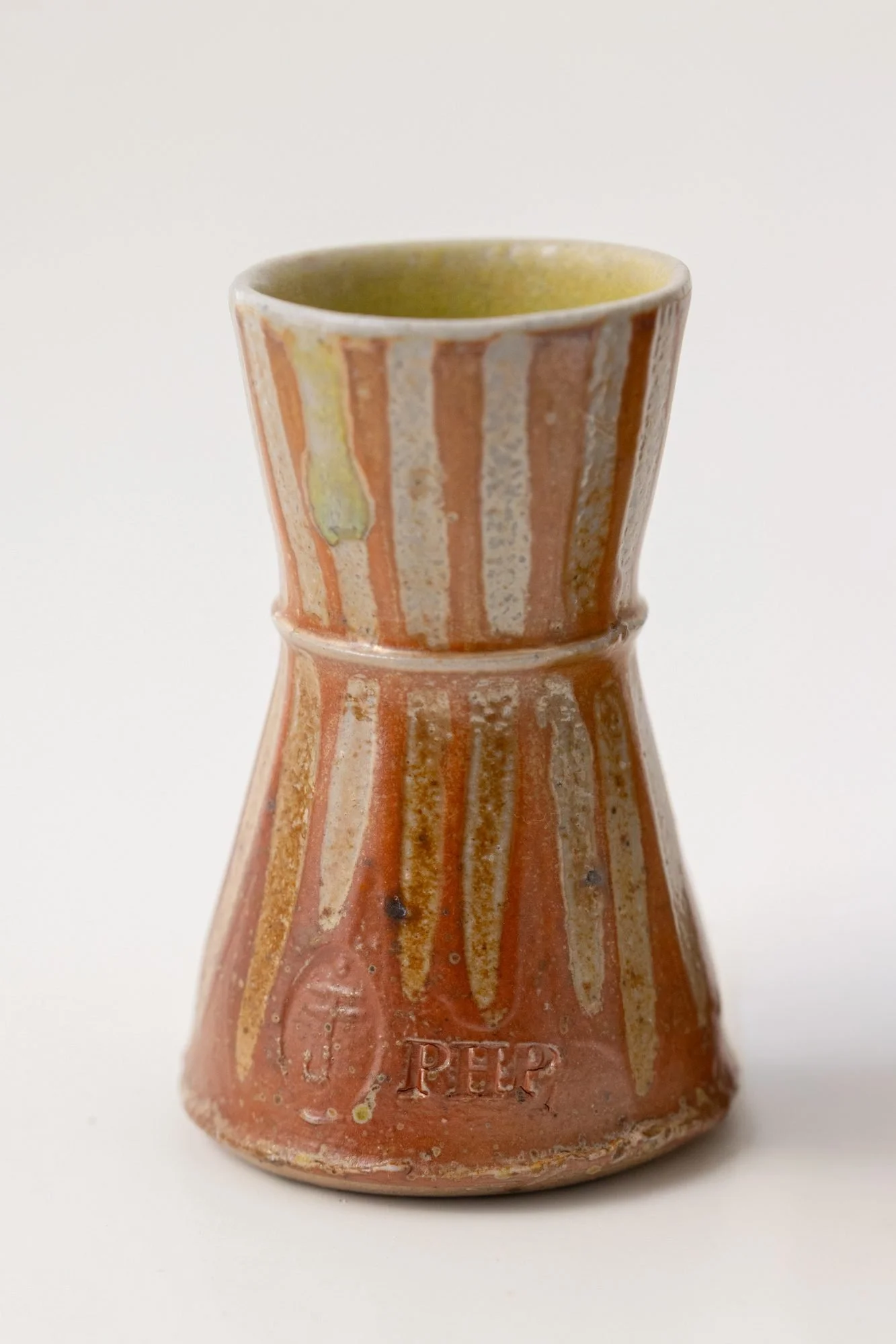 A salt-fired cup with red and white vertical stripes and a stamped mark near its foot