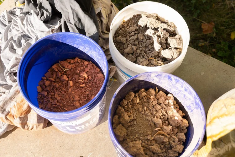 Three buckets of dry wild clay in different colors sitting on a tarp
