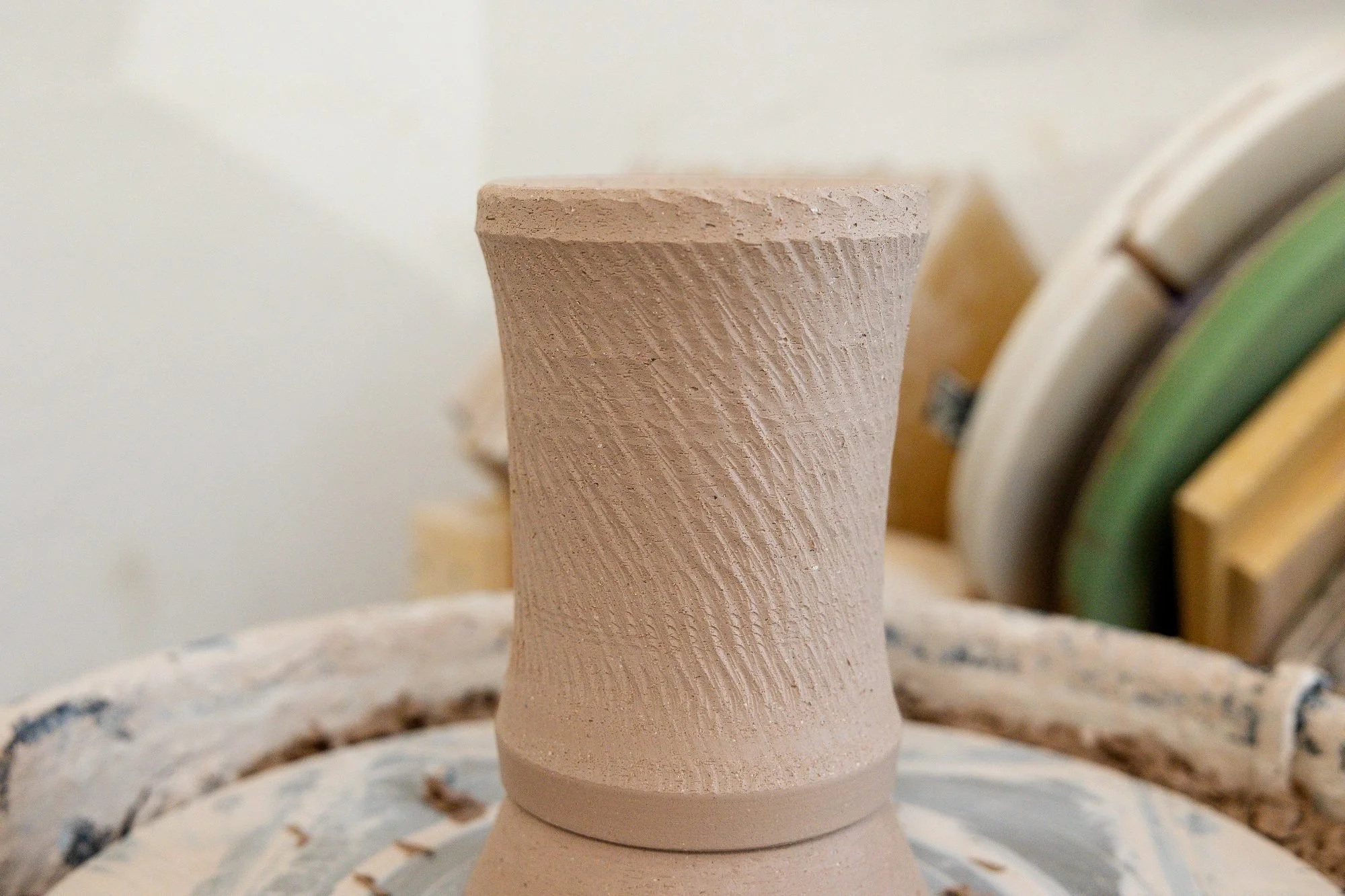 A leather hard textured clay cylinder upside down on the wheel during trimming