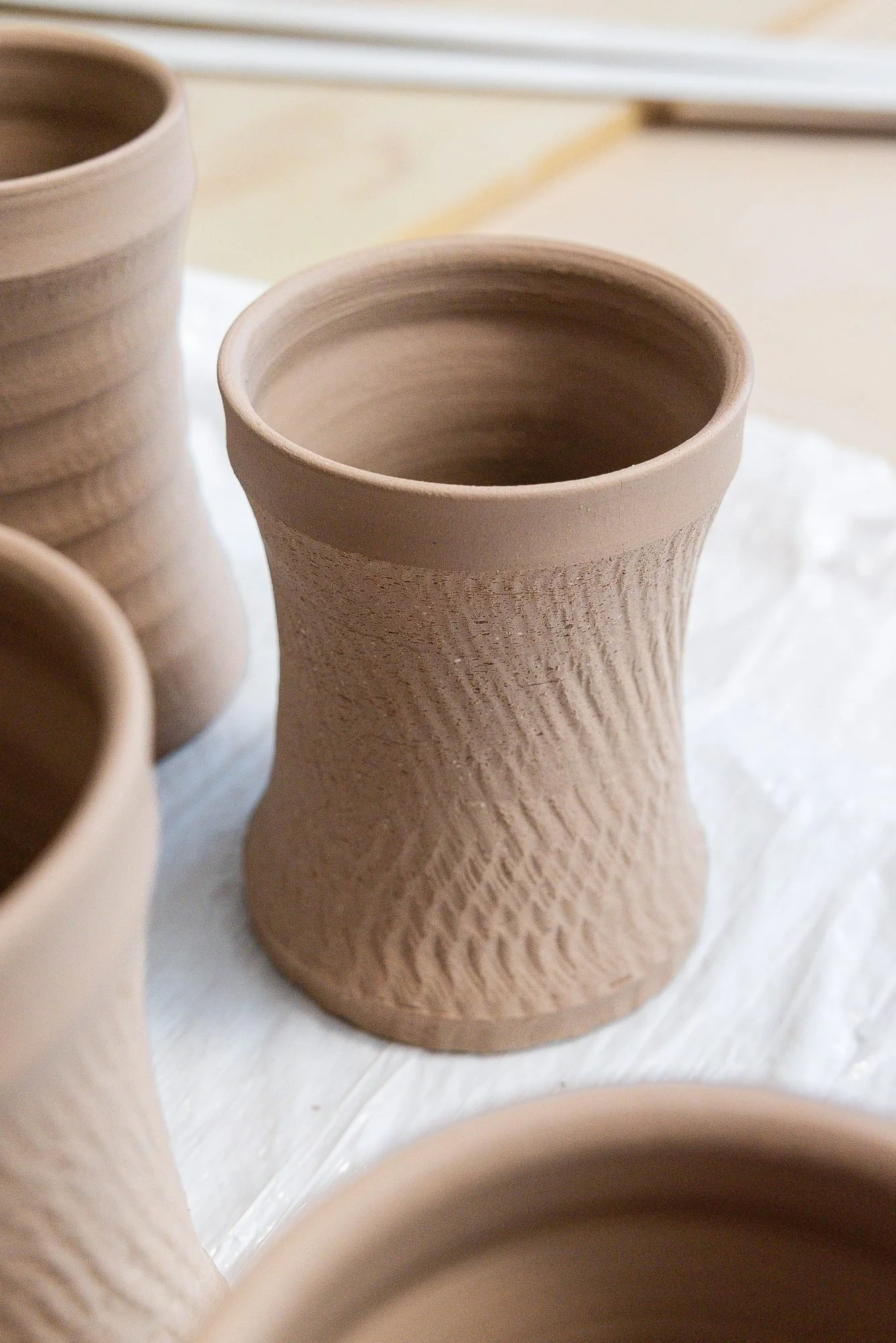 Freshly thrown clay cylinders with textured walls resting on a table