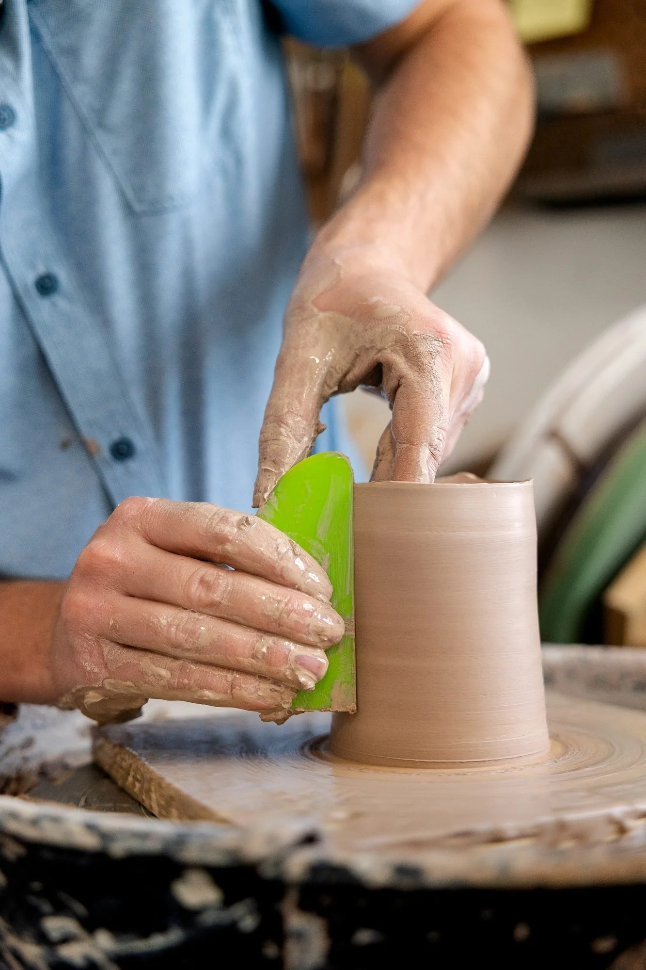 A potter pressing a green rib against a clay cylinder on the wheel