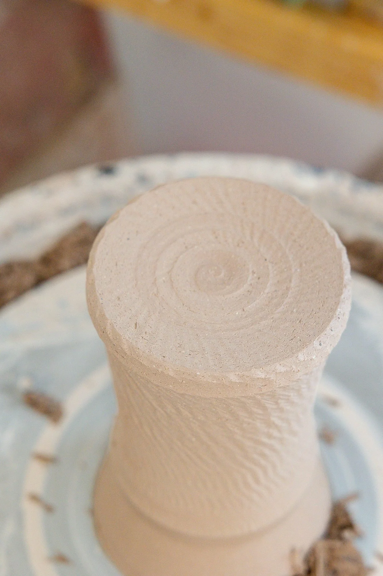 A leather hard clay cylinder upside down on the wheel with a freshly trimmed base
