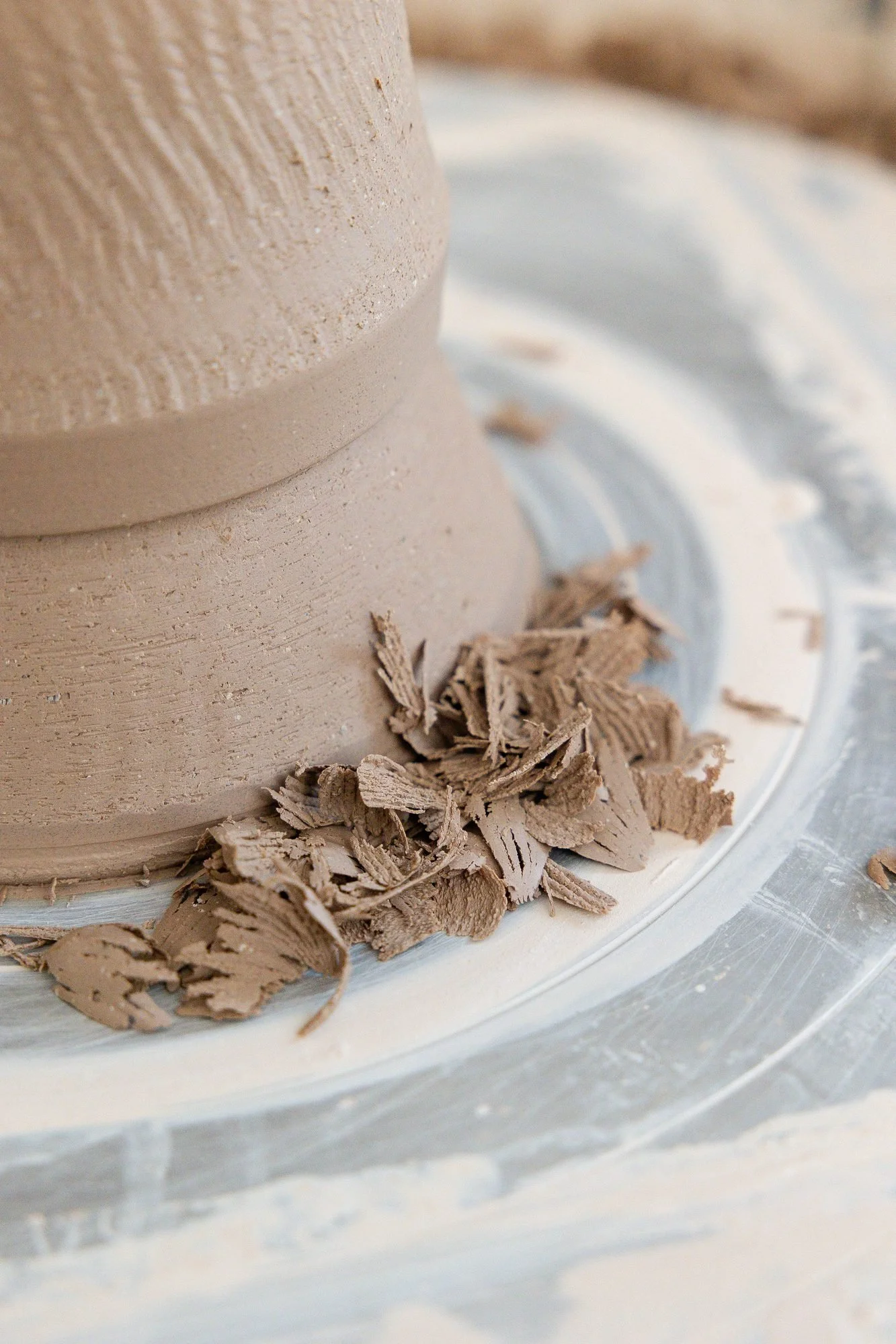 Clay trimmings piled around the foot of an upside down cylinder on the wheel