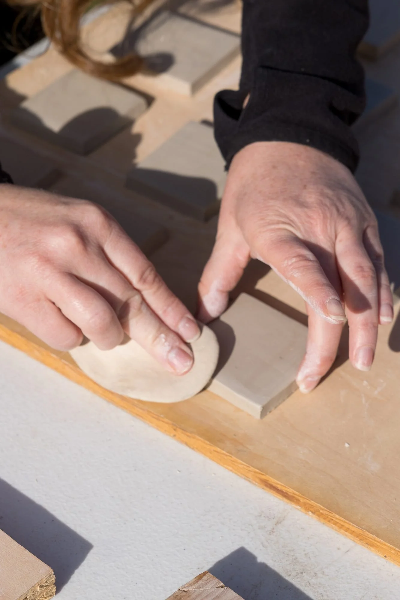 Hands pressing a square clay tile flat on a wooden board