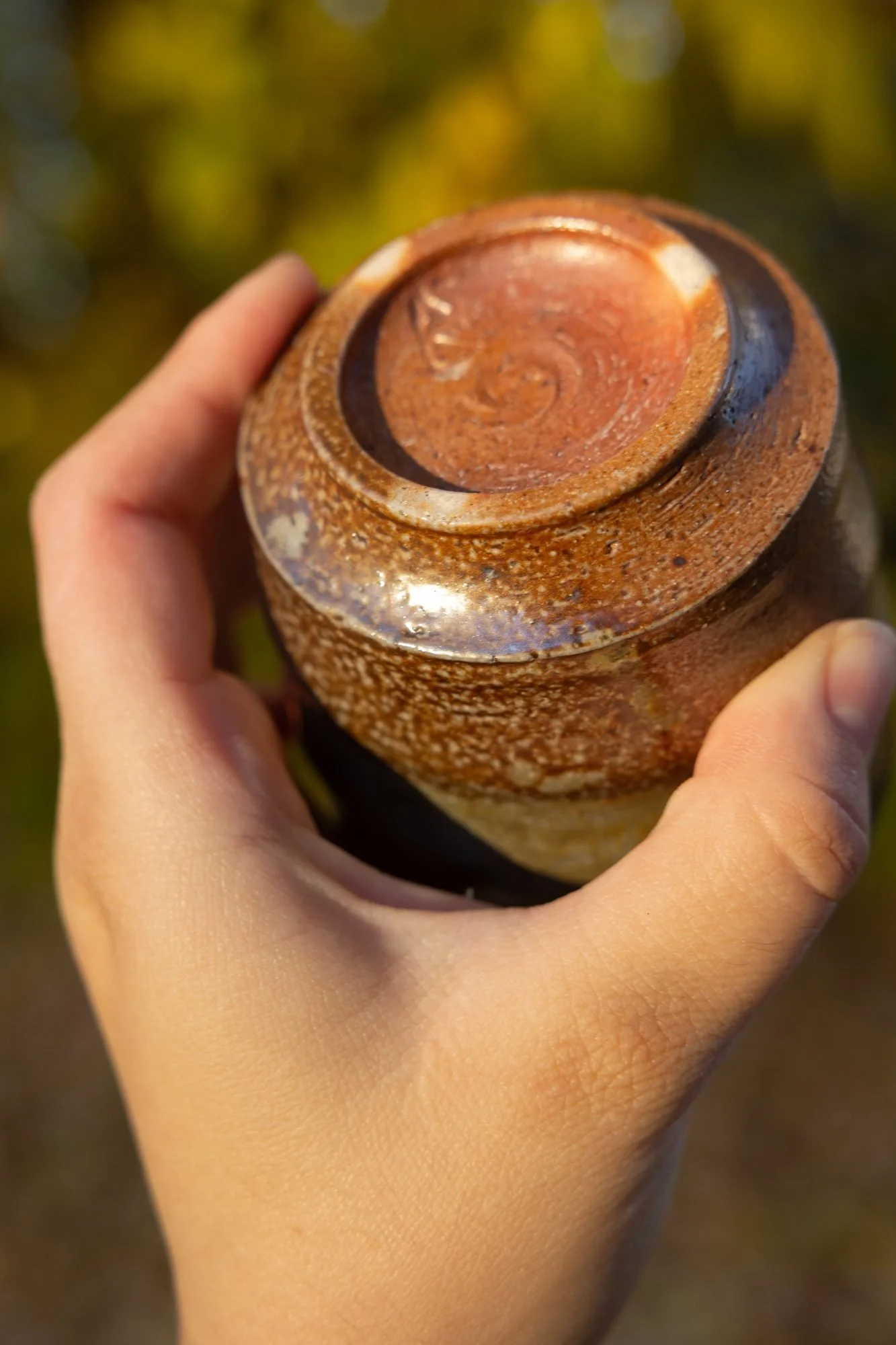 Hand holding a pot upside down to show its iron brown foot against autumn colors