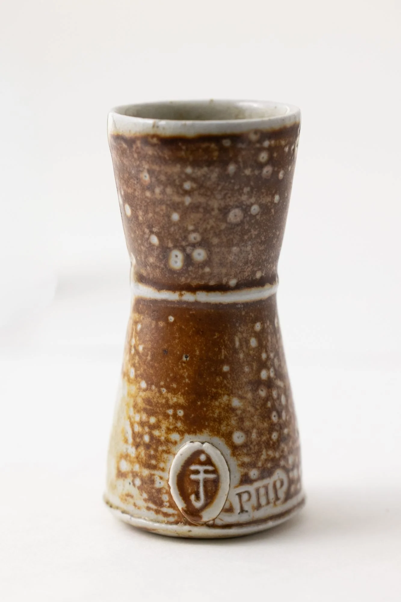 A warm brown speckled pot with a stamped maker's mark near the base, on a white background