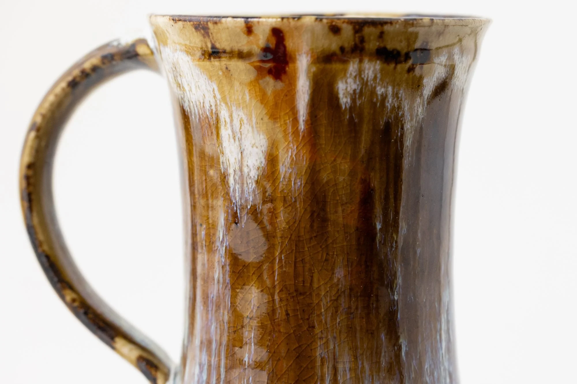 Close view of a mug with amber and white glaze runs and a pulled handle, on a white background