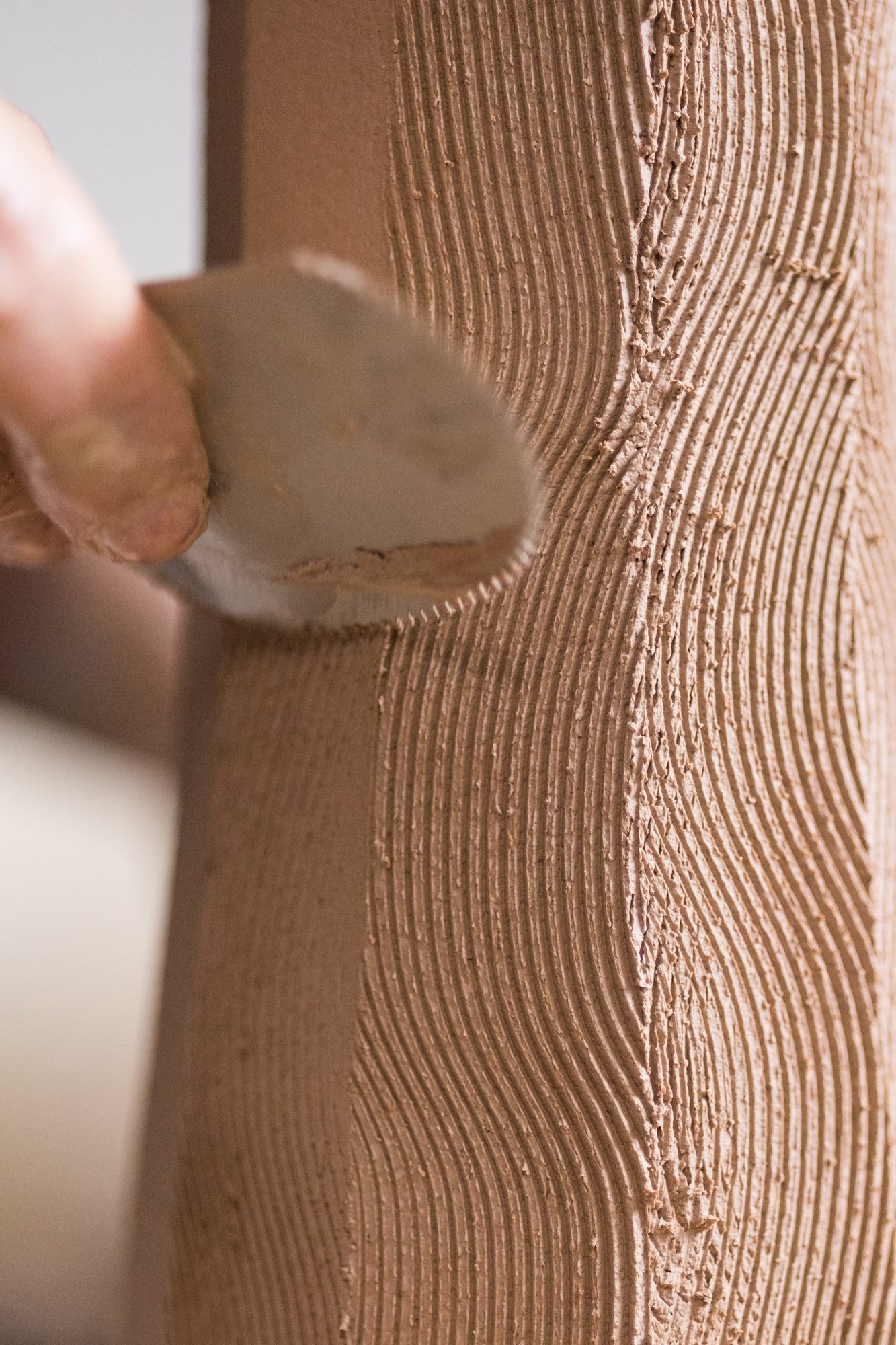 Close view of a rib pressing wavy lines into a wet clay wall