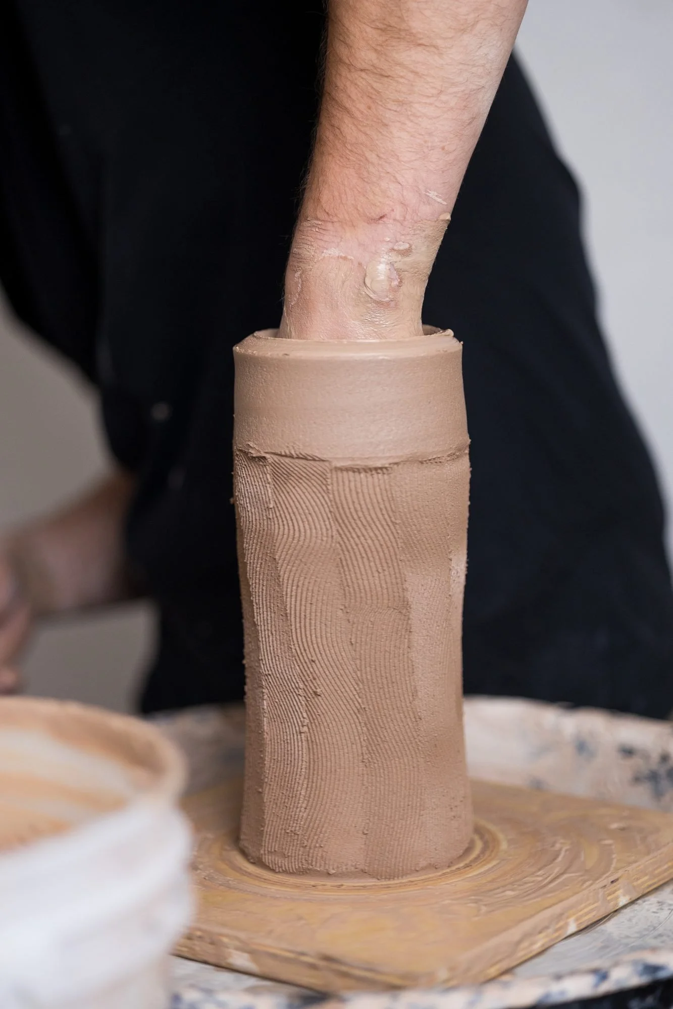 A hand inside a tall ribbed clay form on the wheel
