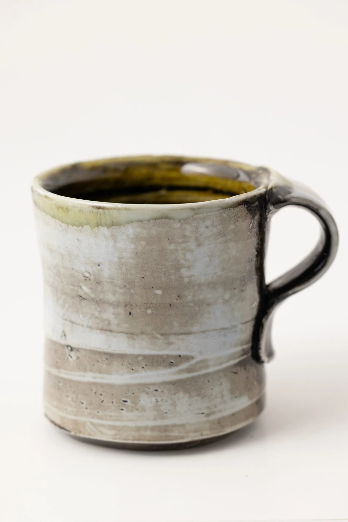 A pale mug with a dark handle and green rim on a white background