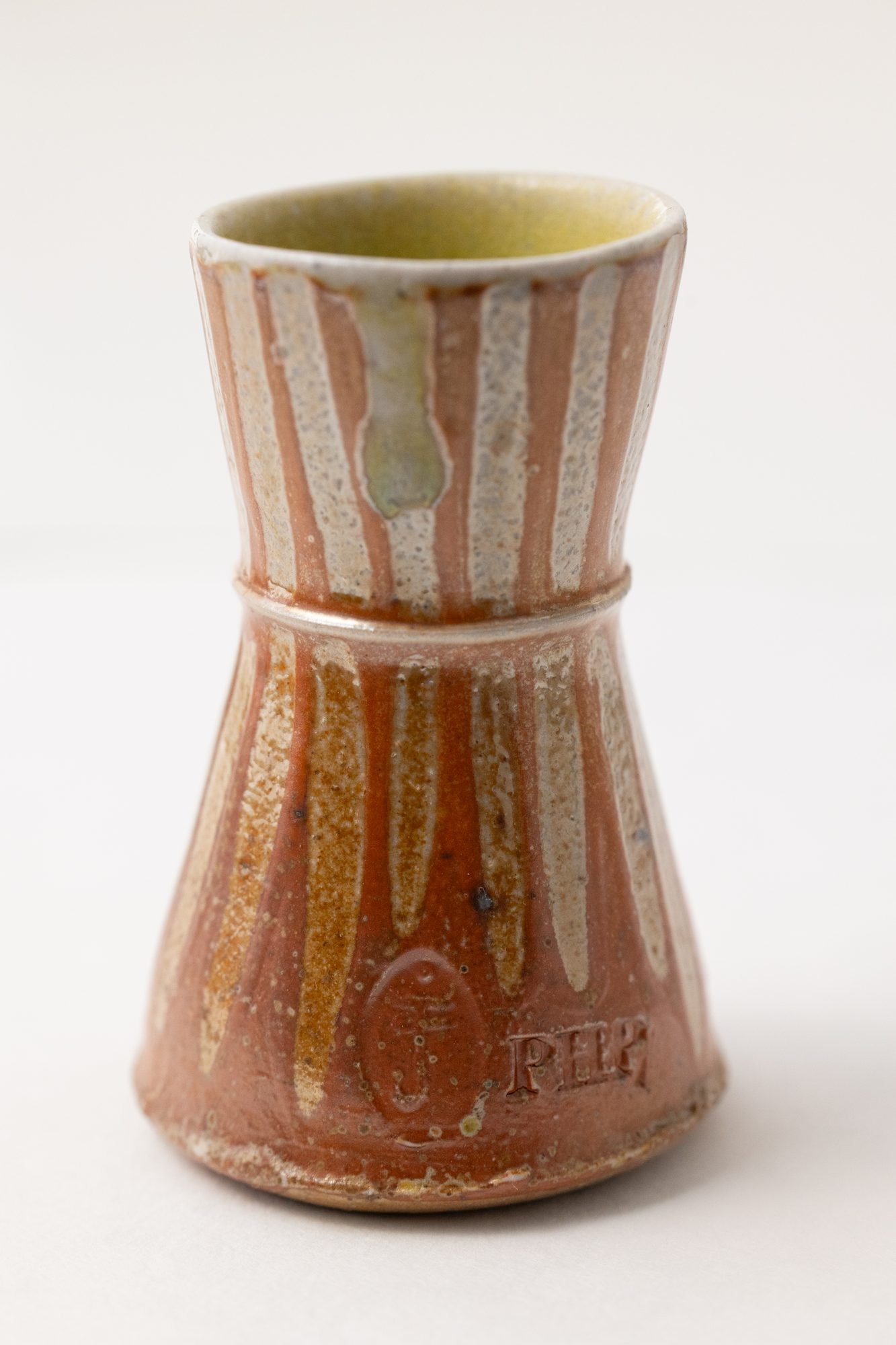 A vase with orange and white vertical stripes on a white background