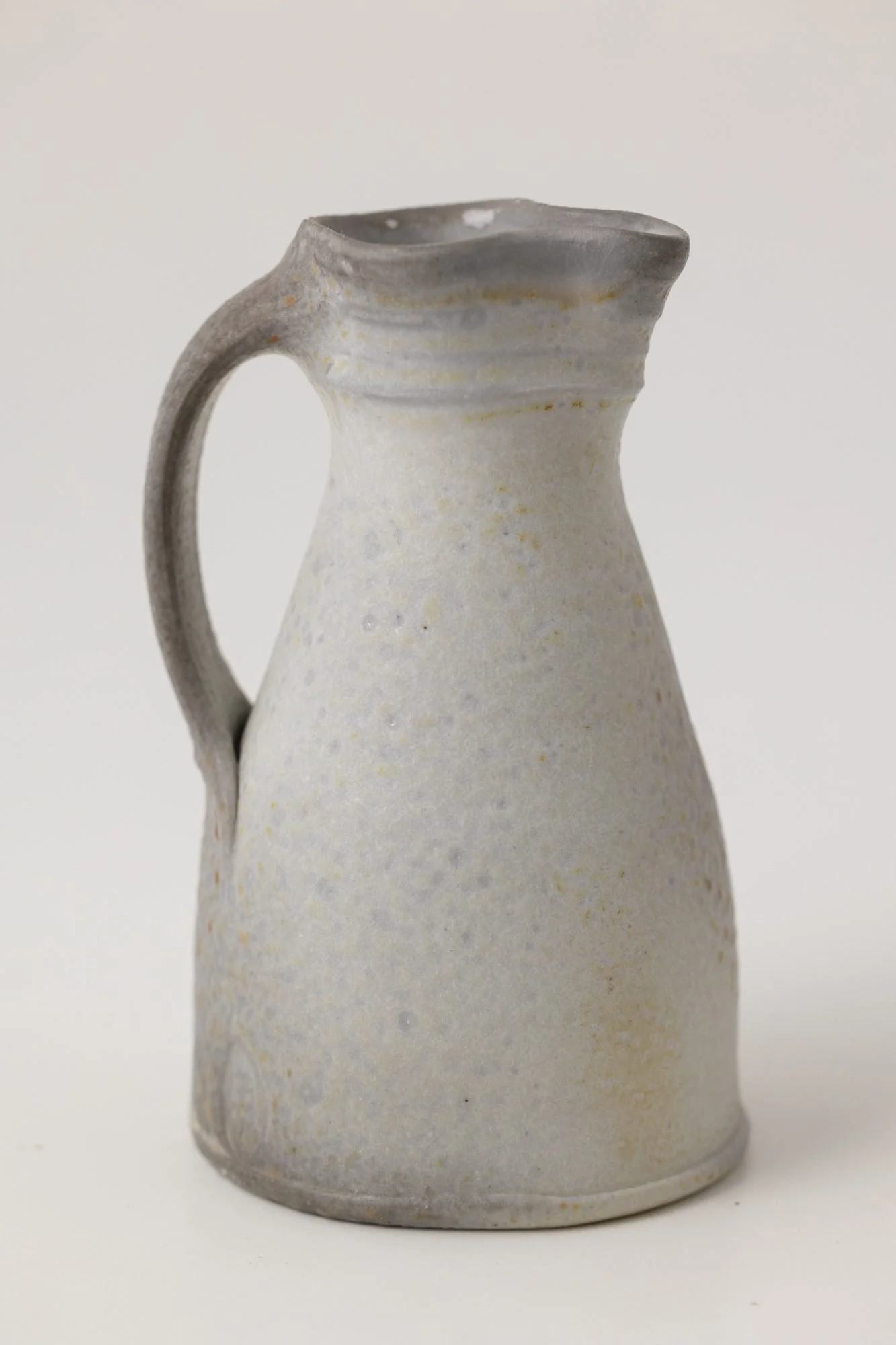 A pale gray pitcher with a soft speckled surface on a white background