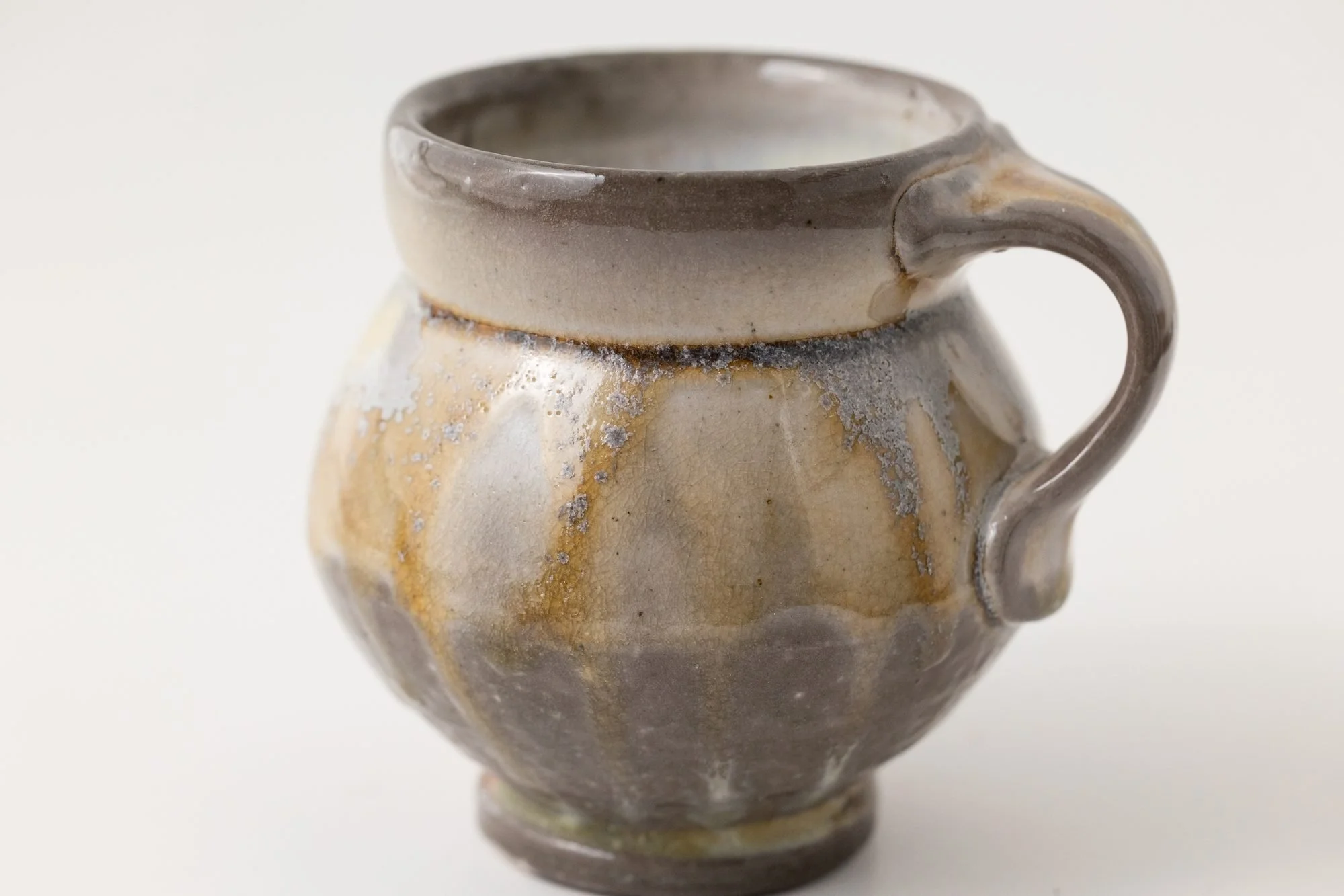 A round mug with a gray rim and amber flashing on its ribbed belly
