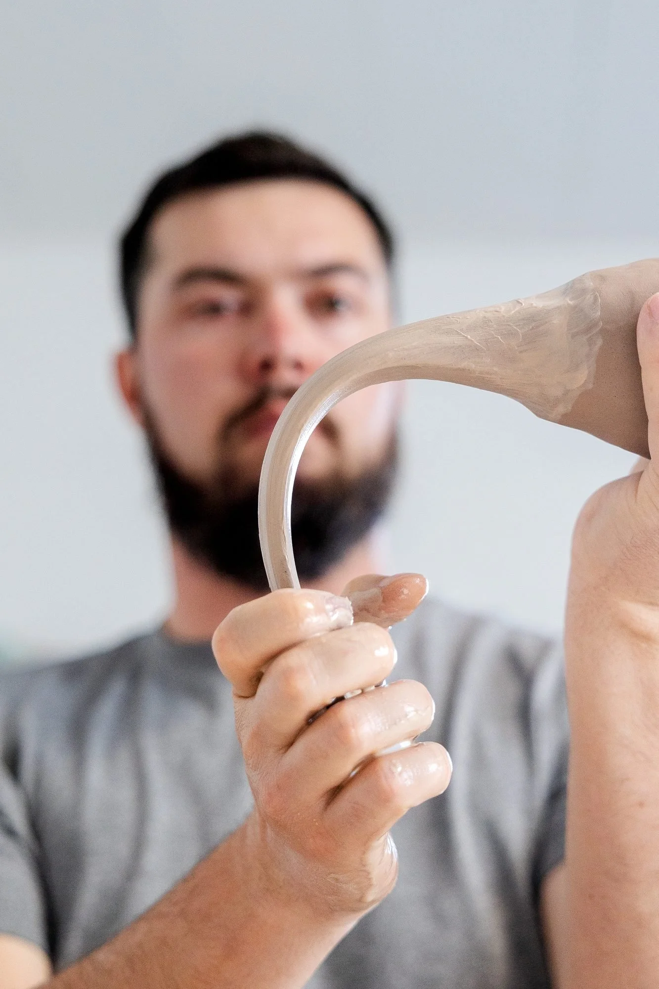 A potter holding up a freshly pulled clay handle bent into an arc