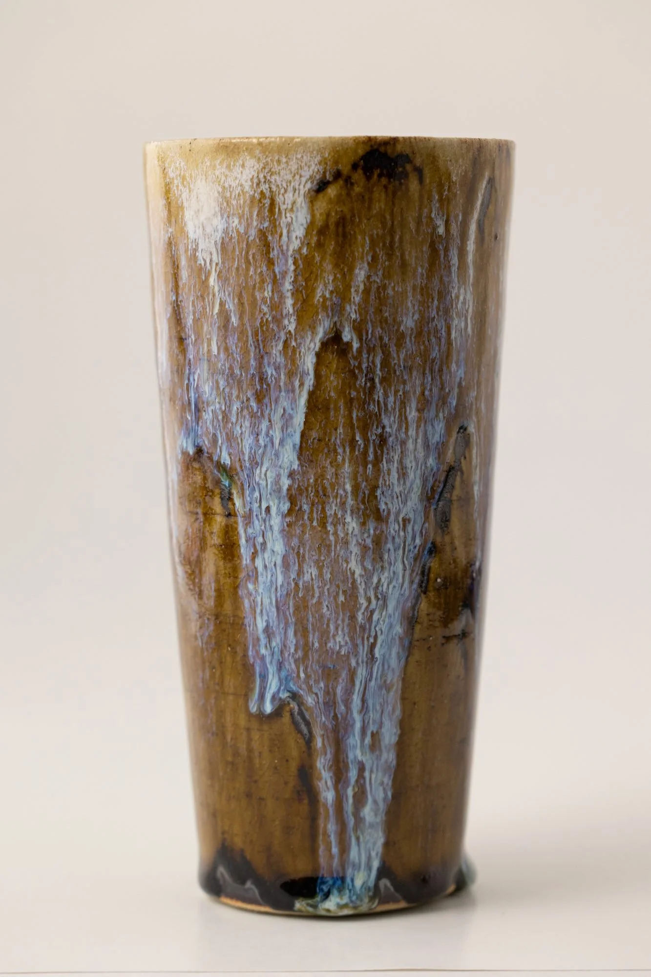 A tall tumbler with amber and pale blue glaze running down its sides