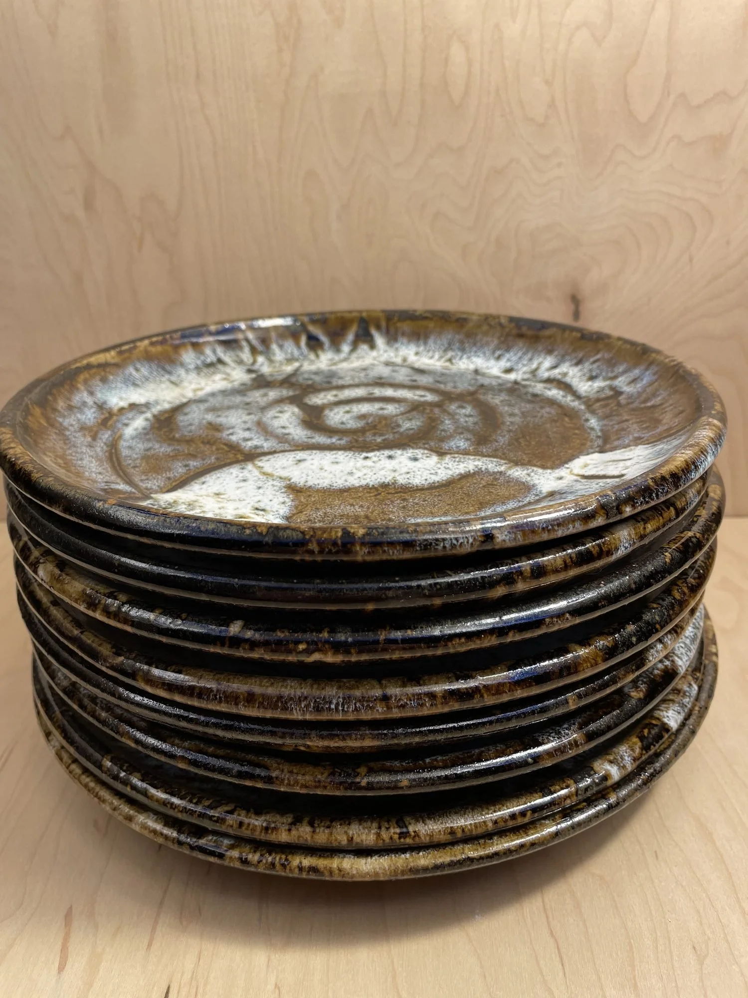 A stack of glazed stoneware plates with white spiral centers and dark brown rims