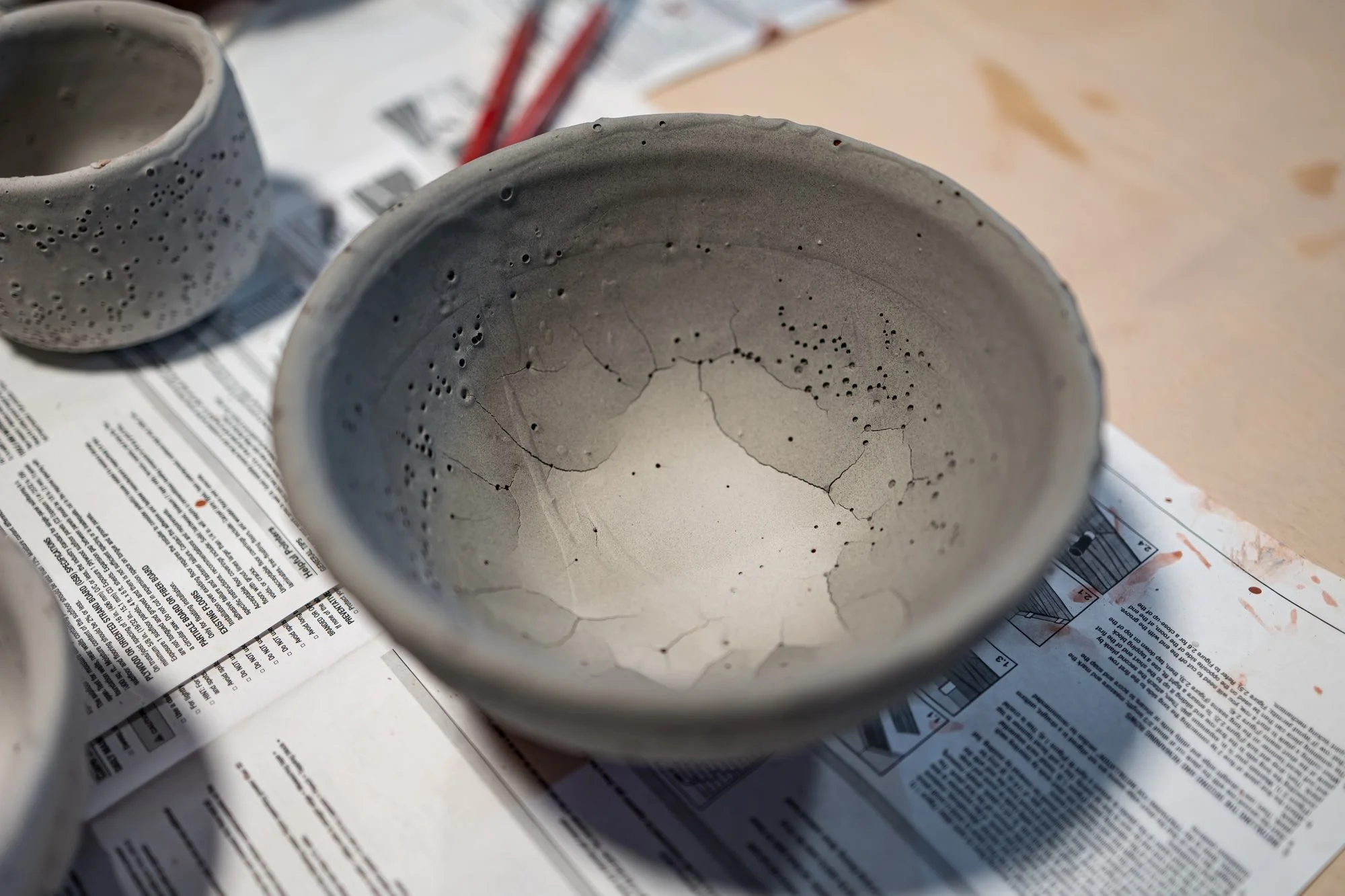 A glazed grey bowl drying on newspaper with other glazed pieces behind it