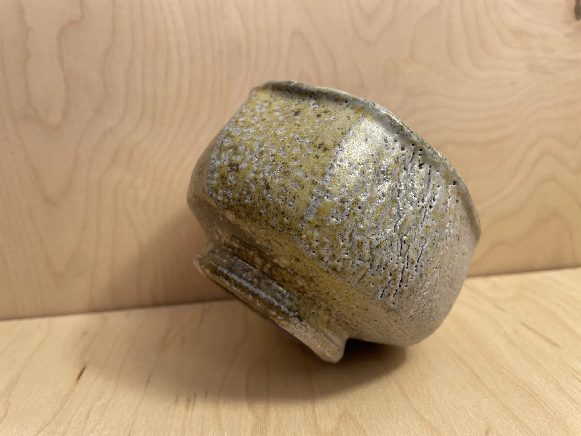 A rough, textured bowl with a pale green and grey surface on a wooden table