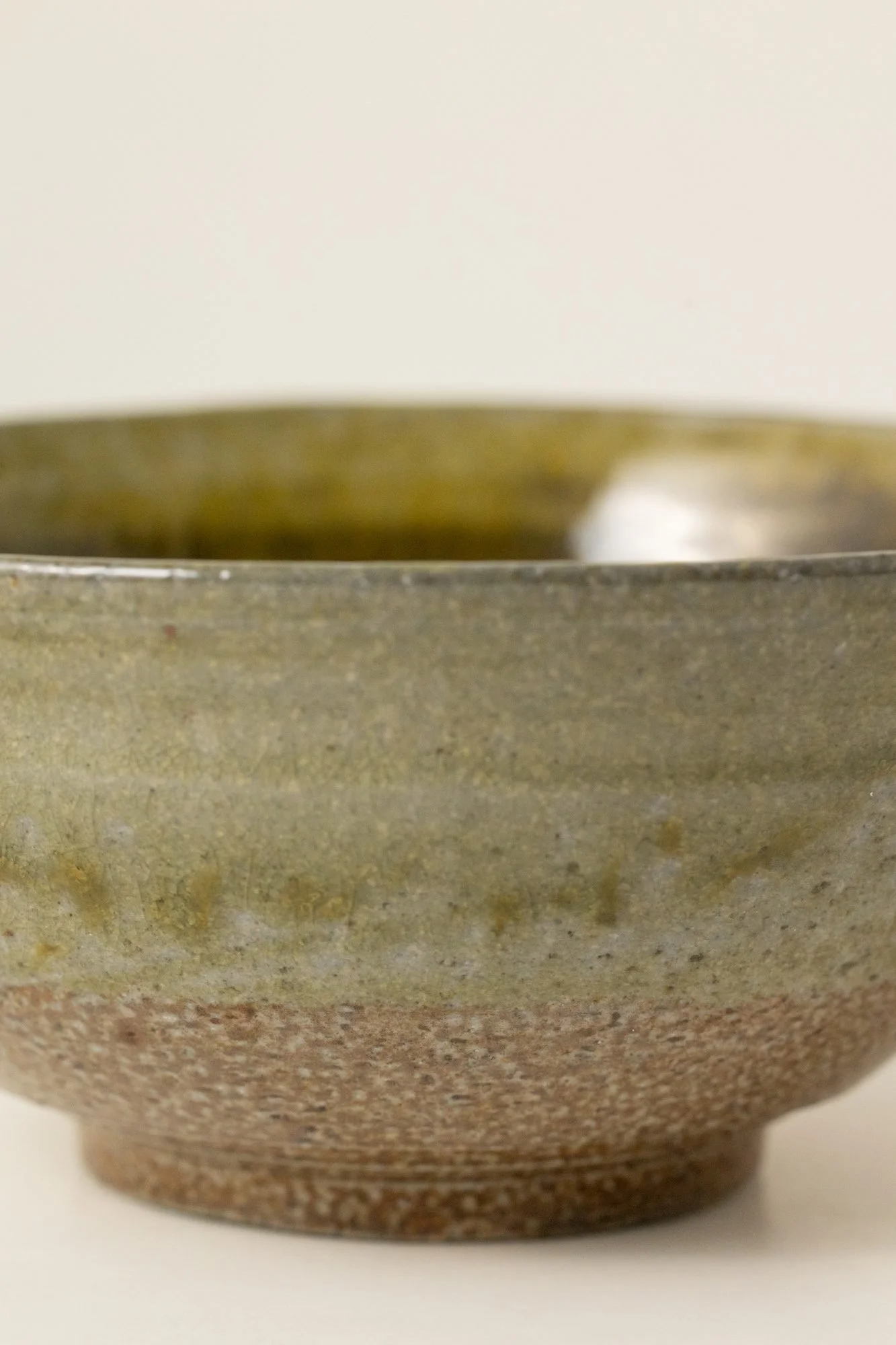 Close view of a green glazed bowl fading into bare speckled clay near the foot