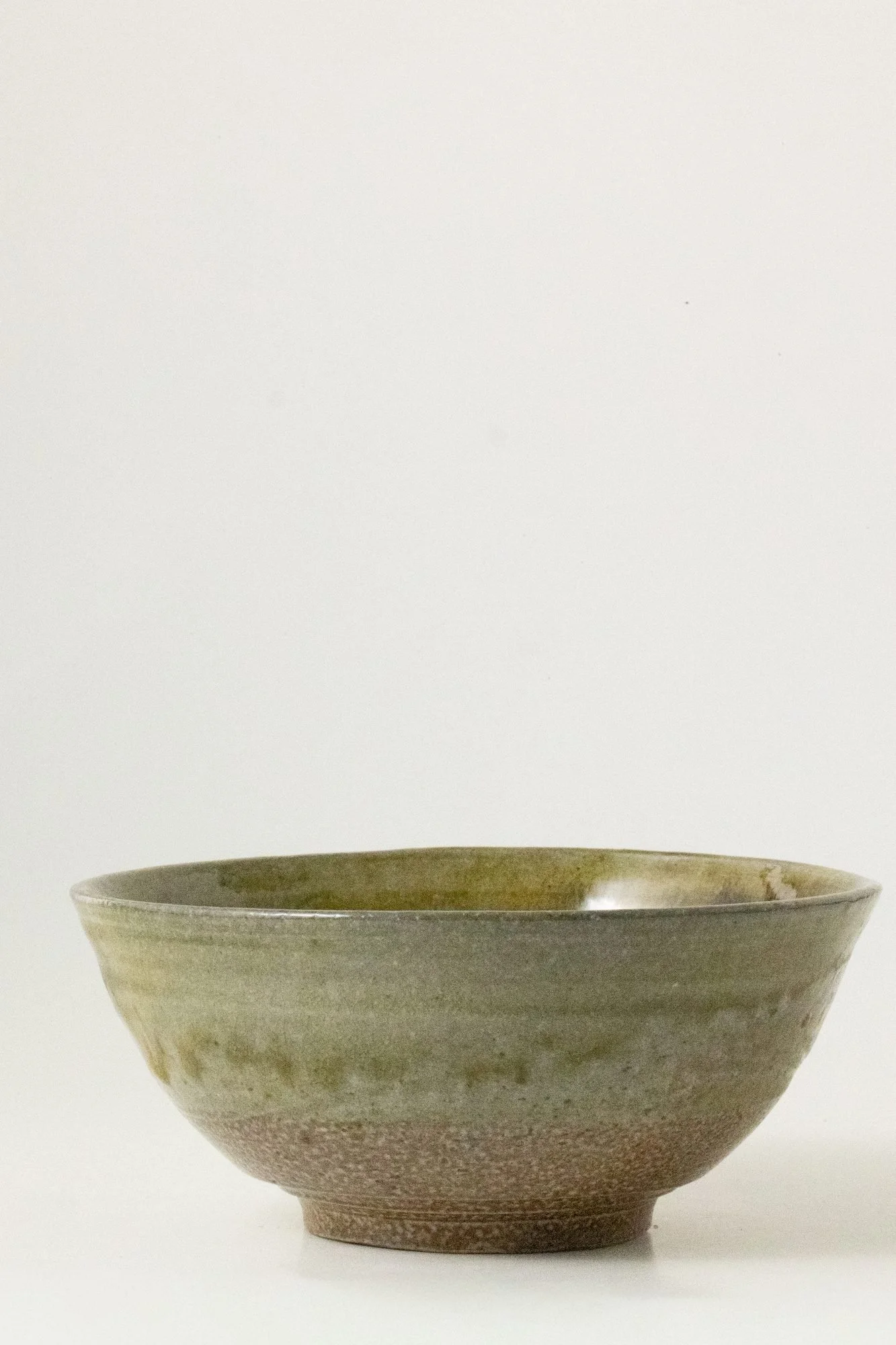 A small green glazed bowl with a darker band above an unglazed foot on a white background
