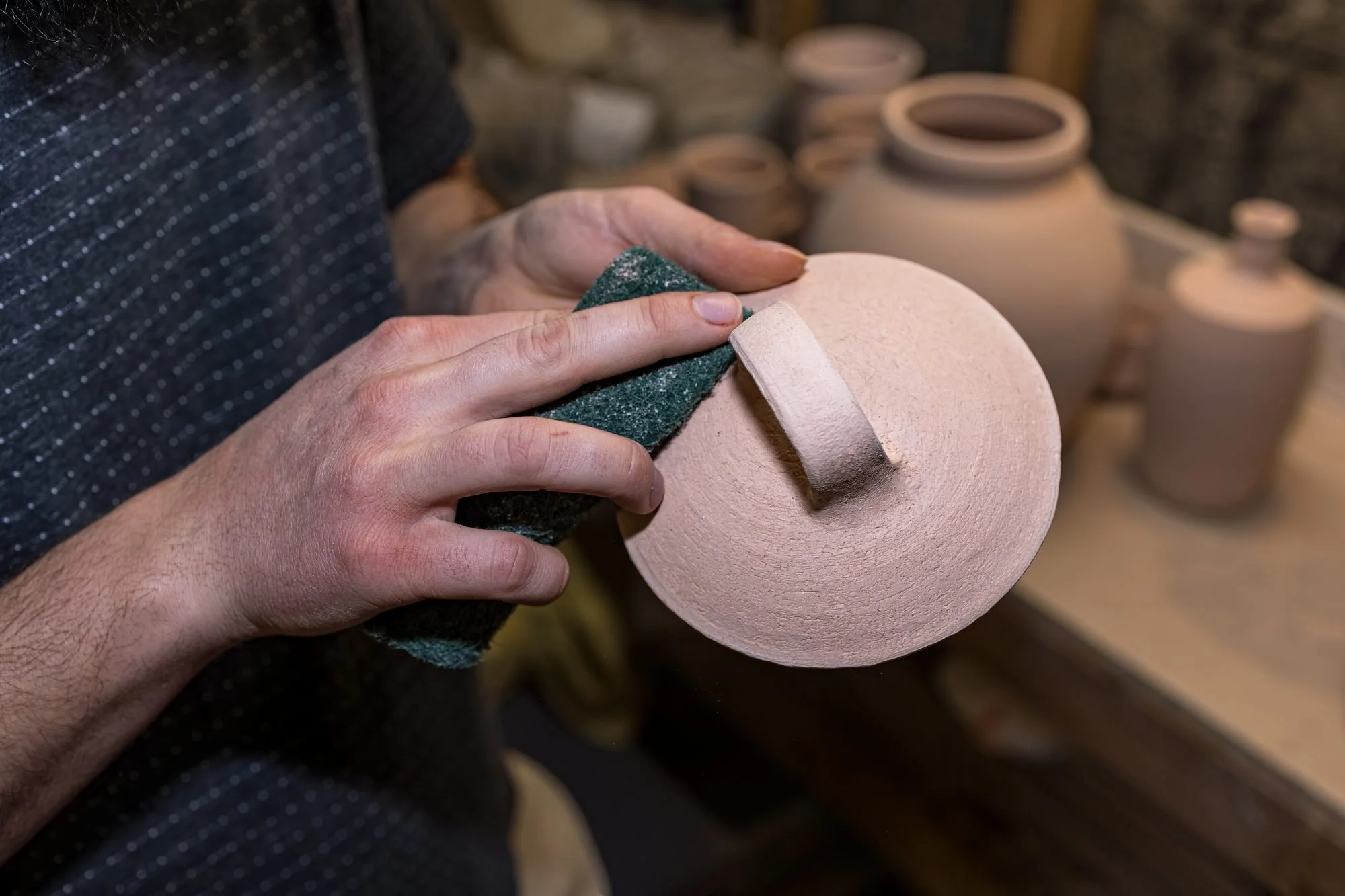 A hand scrubbing the foot of a bisque fired bowl with a green scouring pad