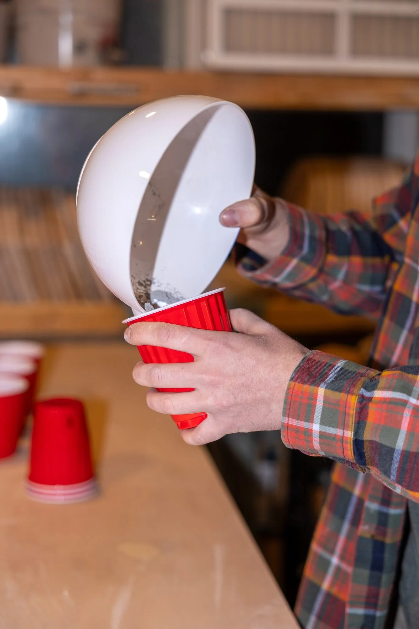 Glaze being poured from a white scoop into a red plastic cup for a test batch