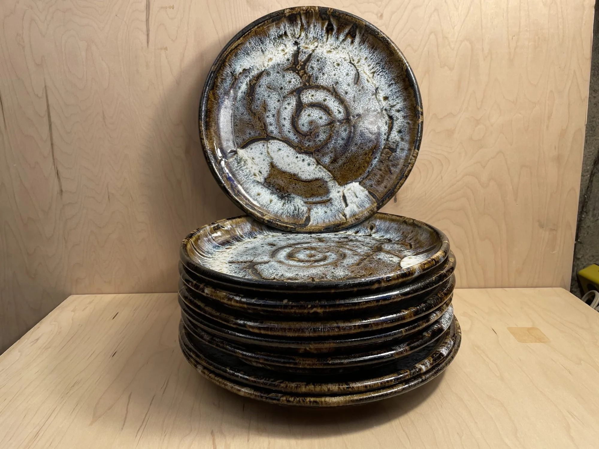 A stack of glazed stoneware plates with one plate standing upright behind, showing a white spiral center