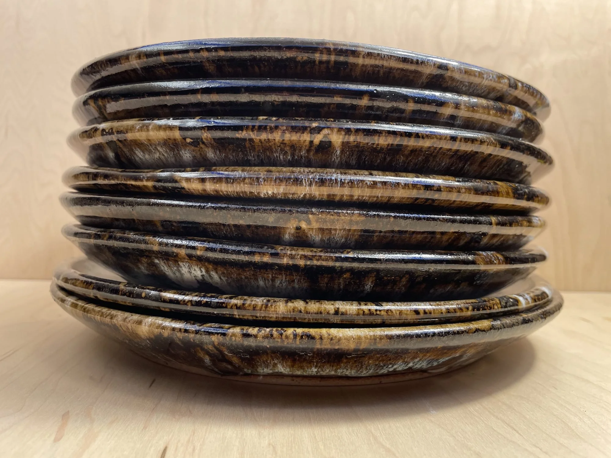 A low stack of dark glazed stoneware plates with white and brown drips at the rims