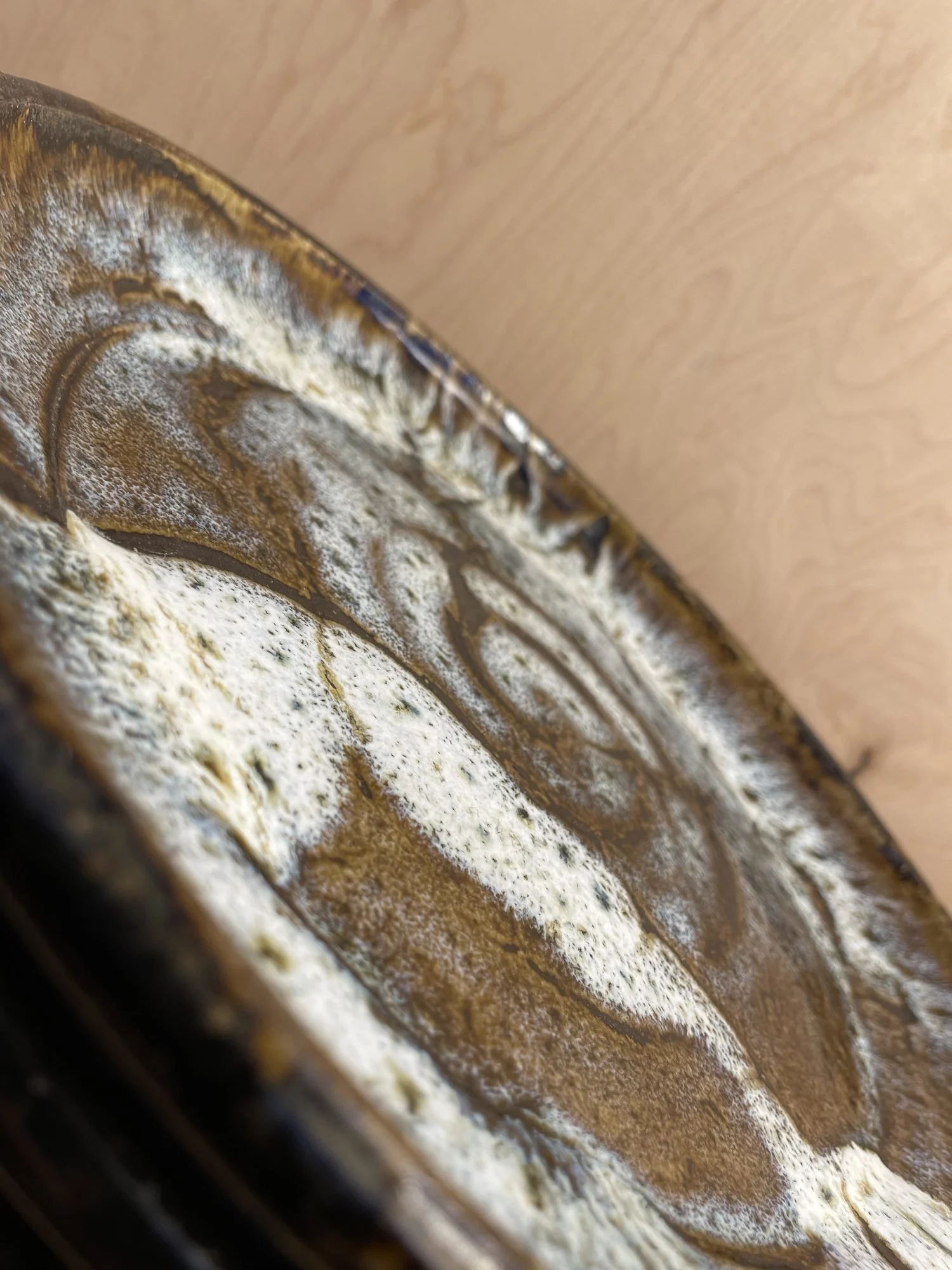 Close view of a glazed plate rim with white glaze breaking over brown