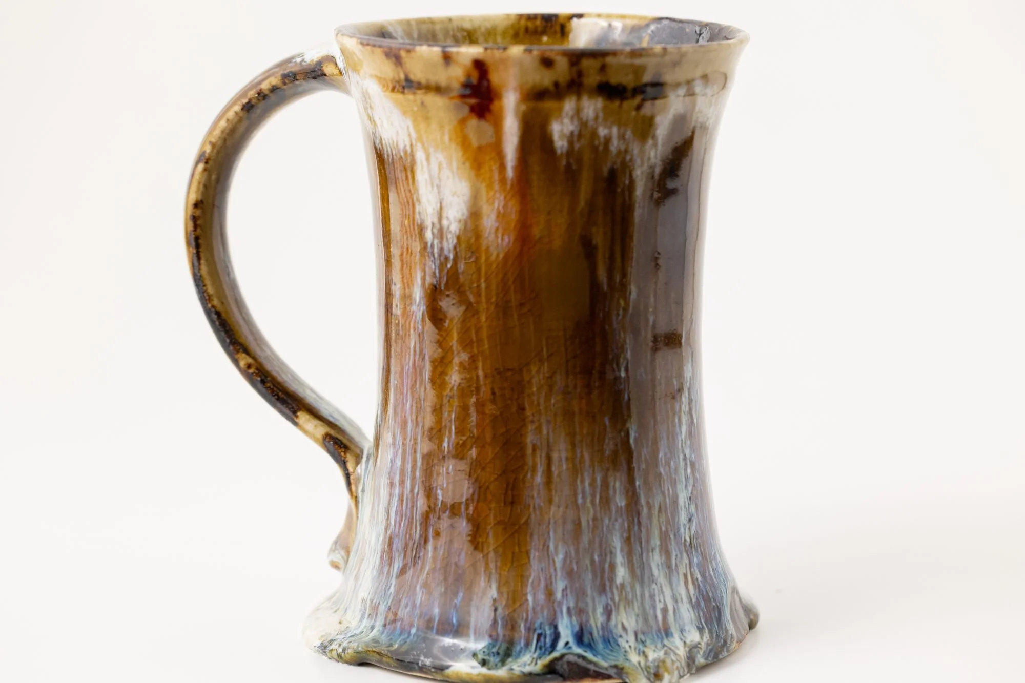 A tall mug with amber glaze breaking to pale blue near the foot on a white background