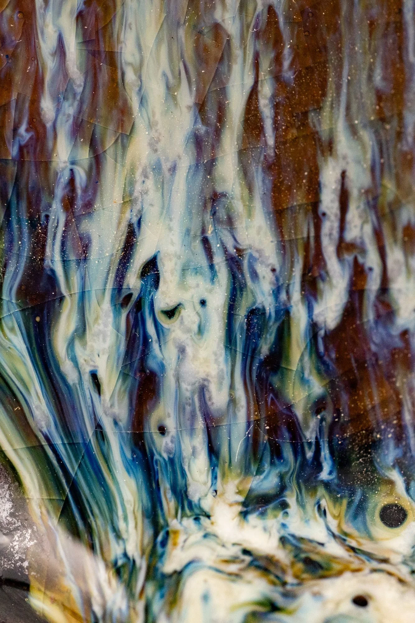 Extreme close view of blue, white and brown glaze running in streaks down a pot