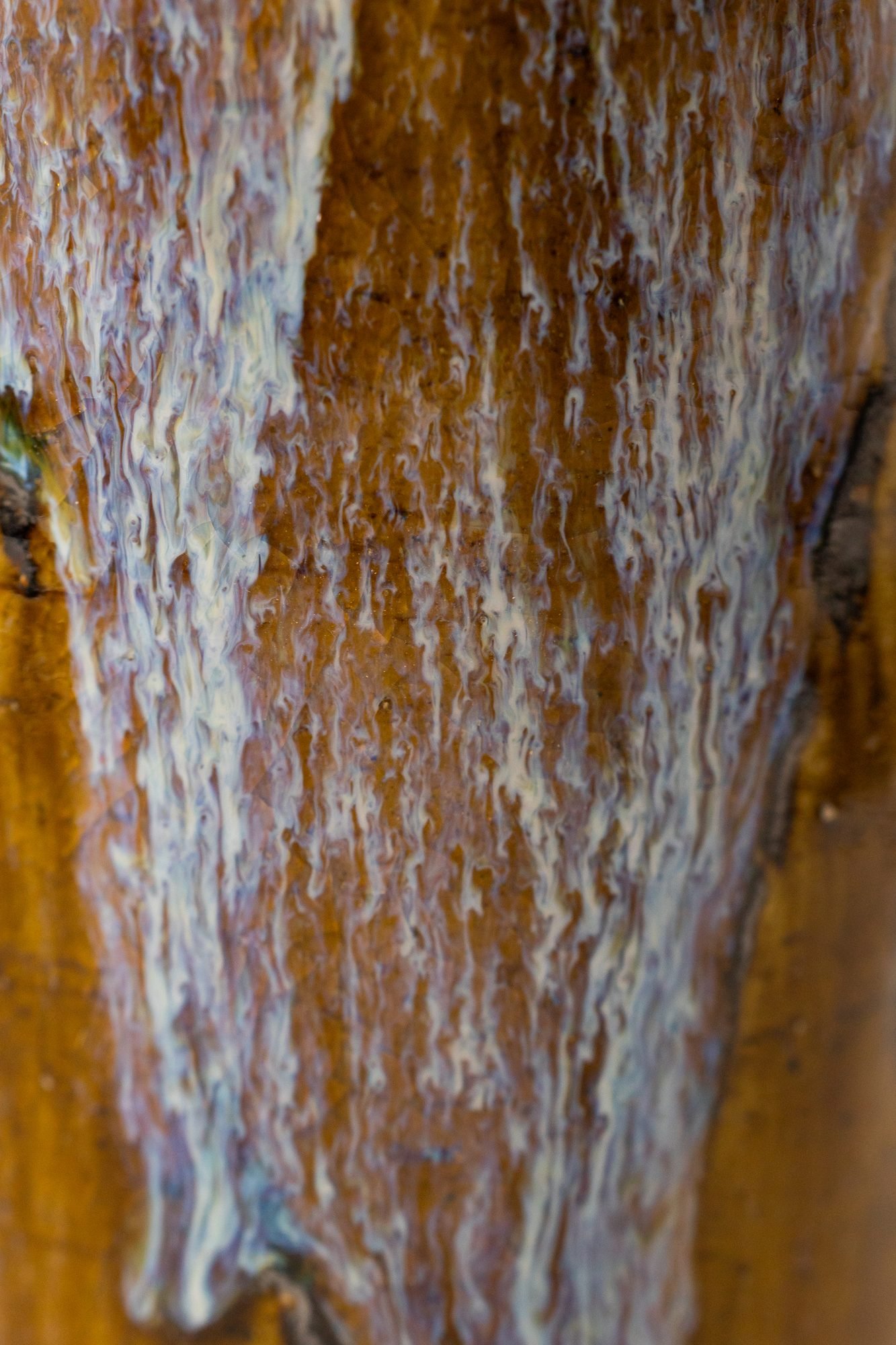 Close view of pale blue glaze running over a brown surface near the foot of a tumbler