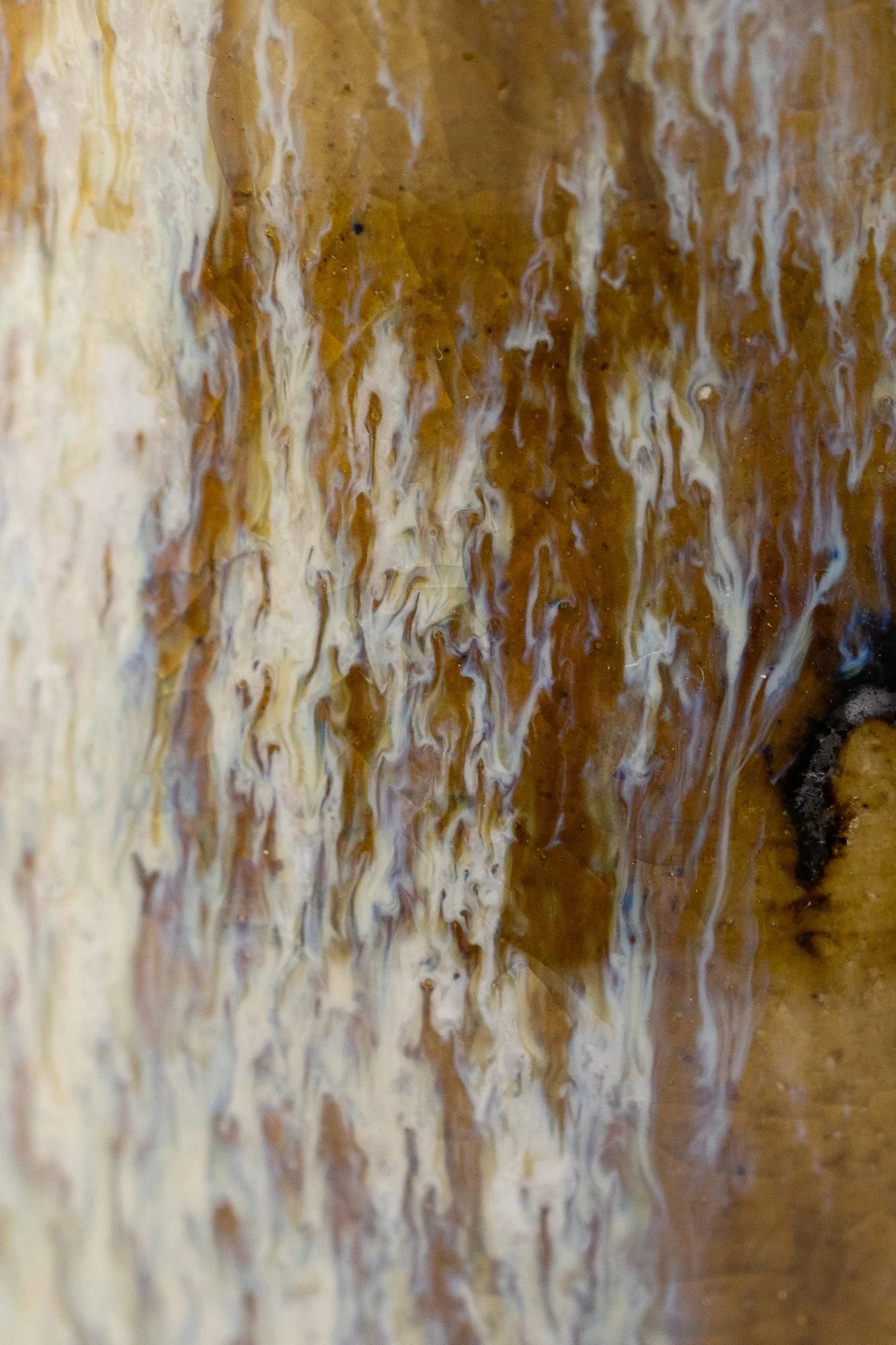 Close view of a cream and brown glazed surface with fine streaks and texture