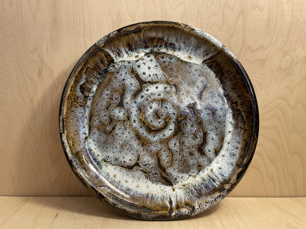 A round glazed stoneware plate with a white spiral center and brown rim standing on a wooden table
