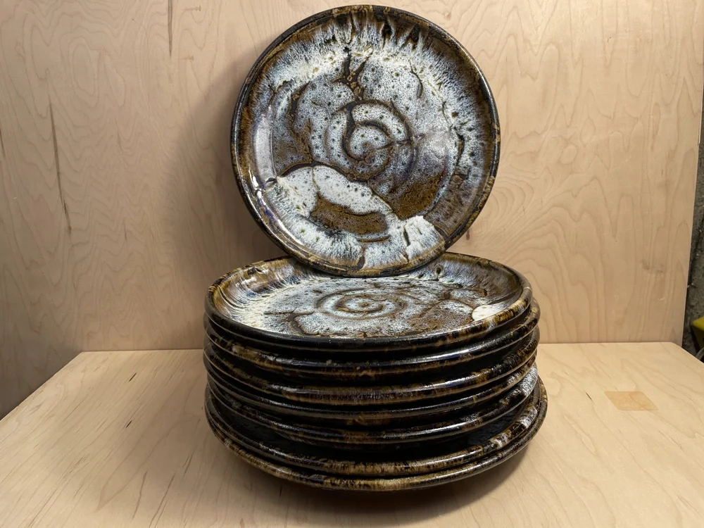 A tall stack of glazed plates with one plate standing upright behind it