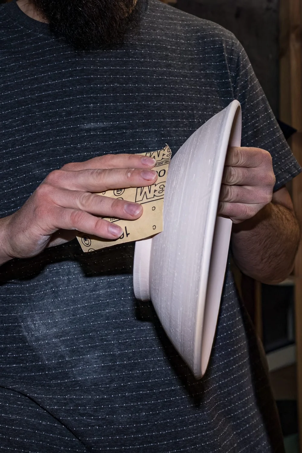 A hand sanding the rim of a wide bisque fired plate