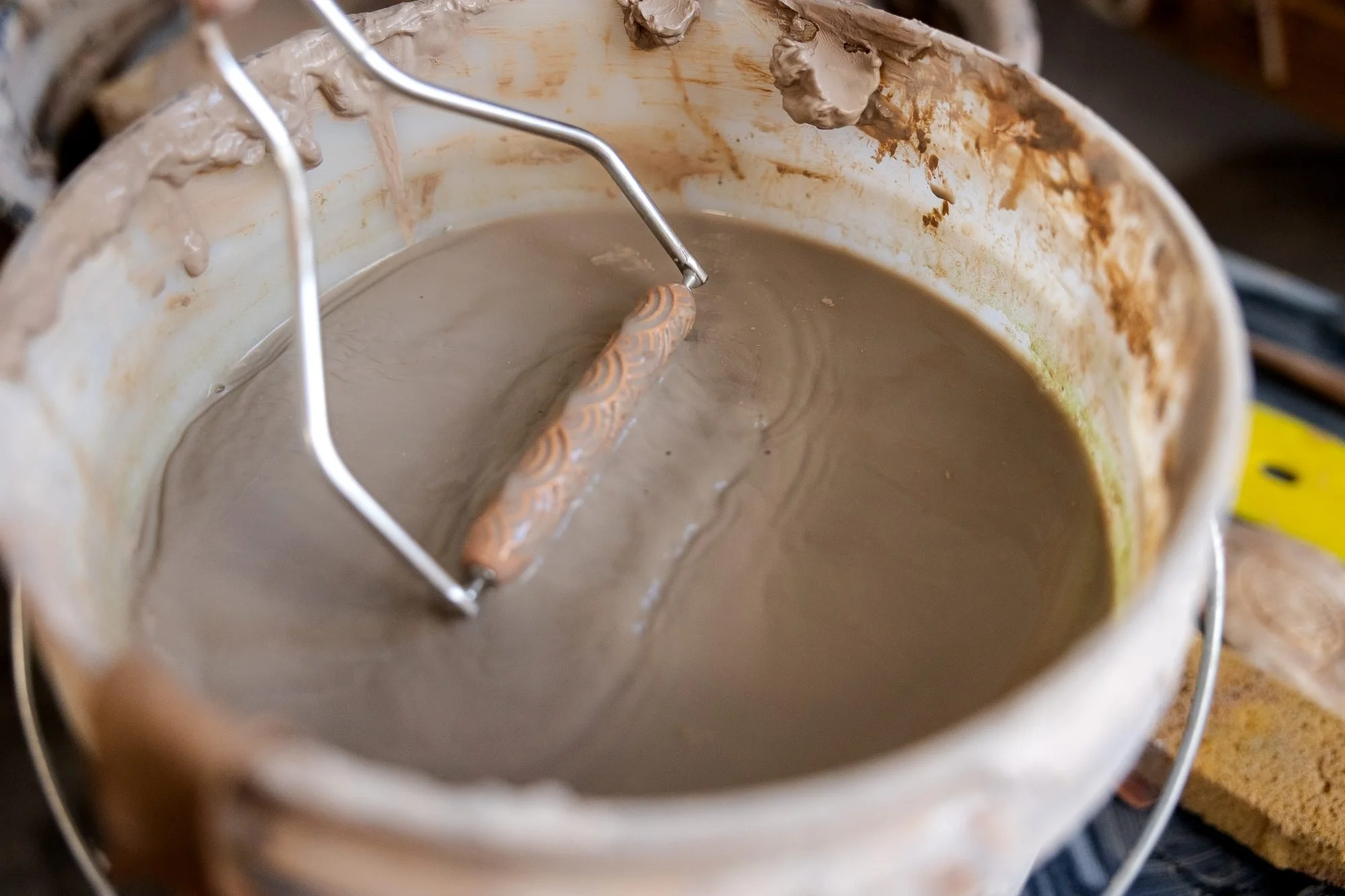 A bucket of clay slurry with a metal mixing paddle resting in it
