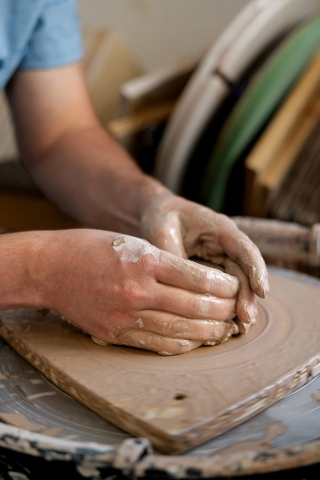 Two hands pressing a lump of clay down onto a wooden bat on the wheel