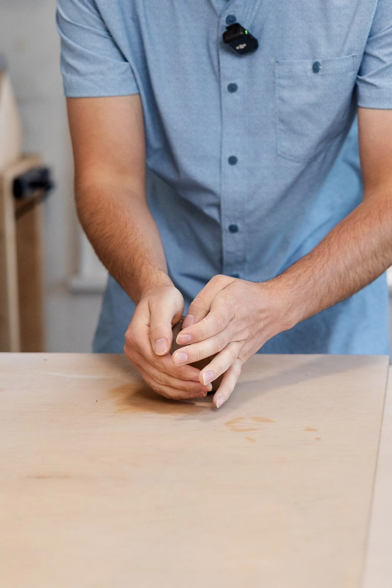 Adam's hands working a small lump of clay on a wooden table