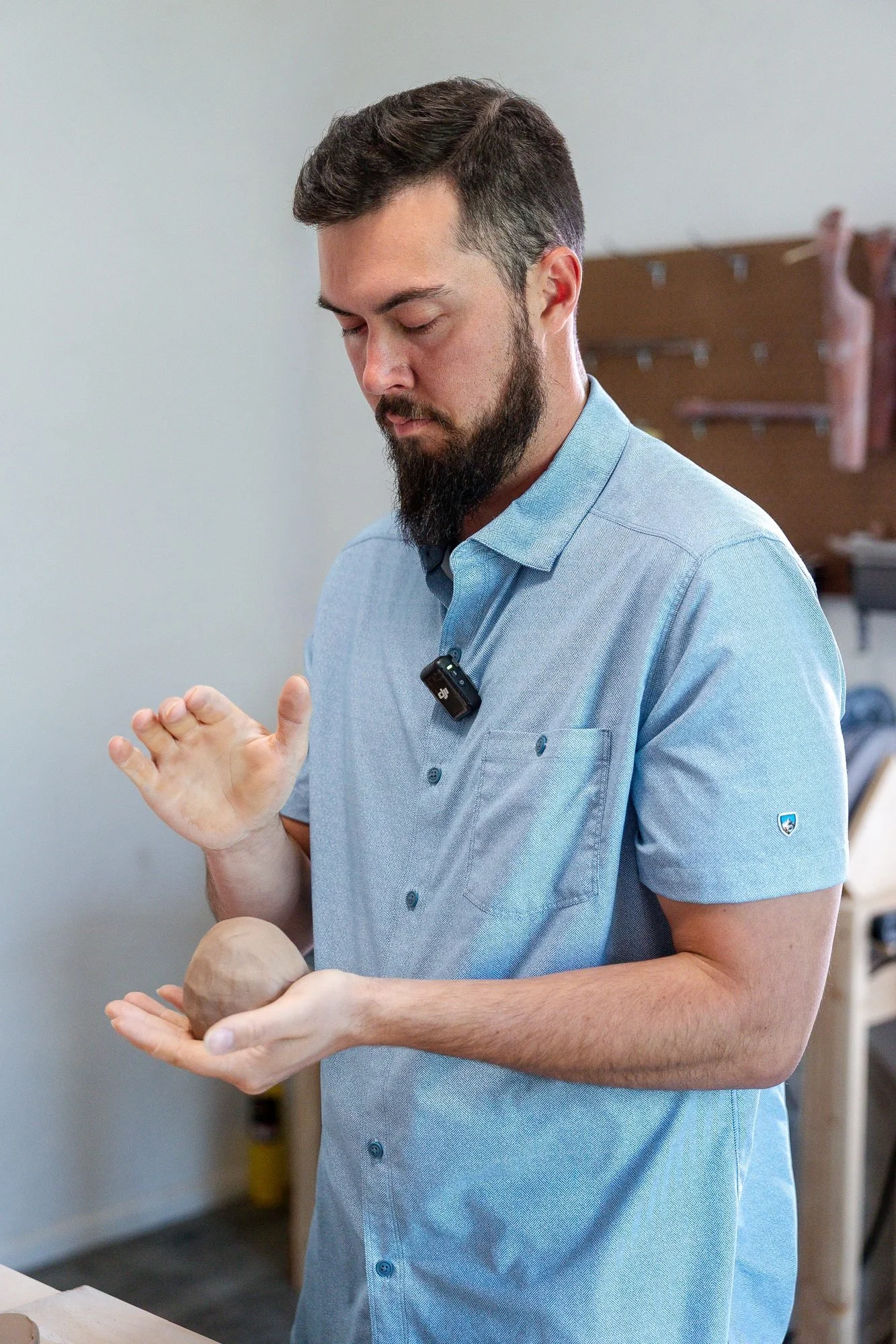 Adam in a blue shirt holding a ball of clay in his palm in the studio