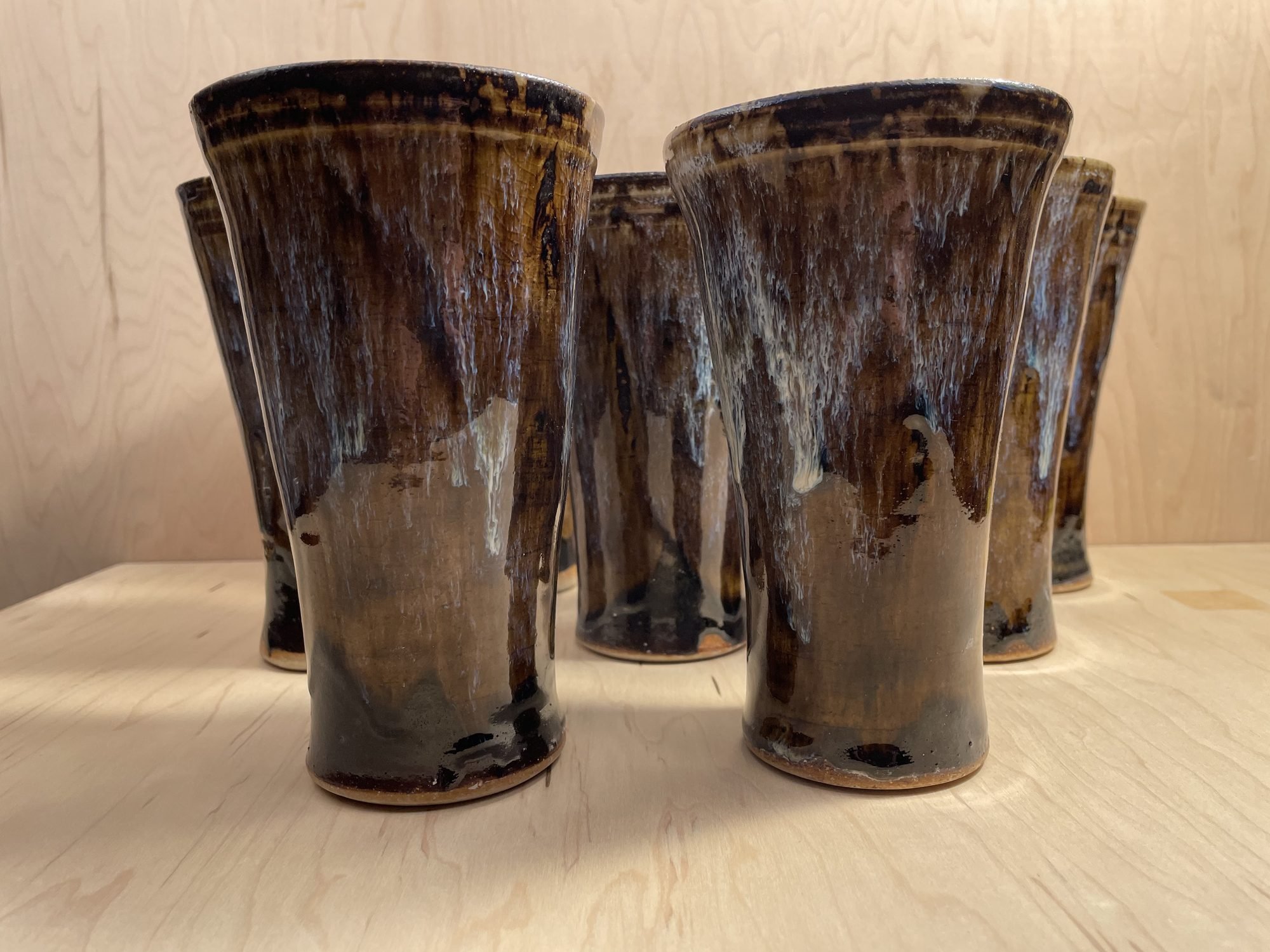 A group of tall glazed tumblers with brown and blue drips standing on a wooden table