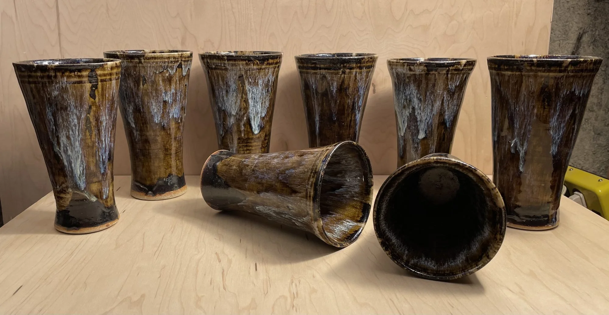 A row of glazed tumblers on a table with two lying on their sides showing dark interiors