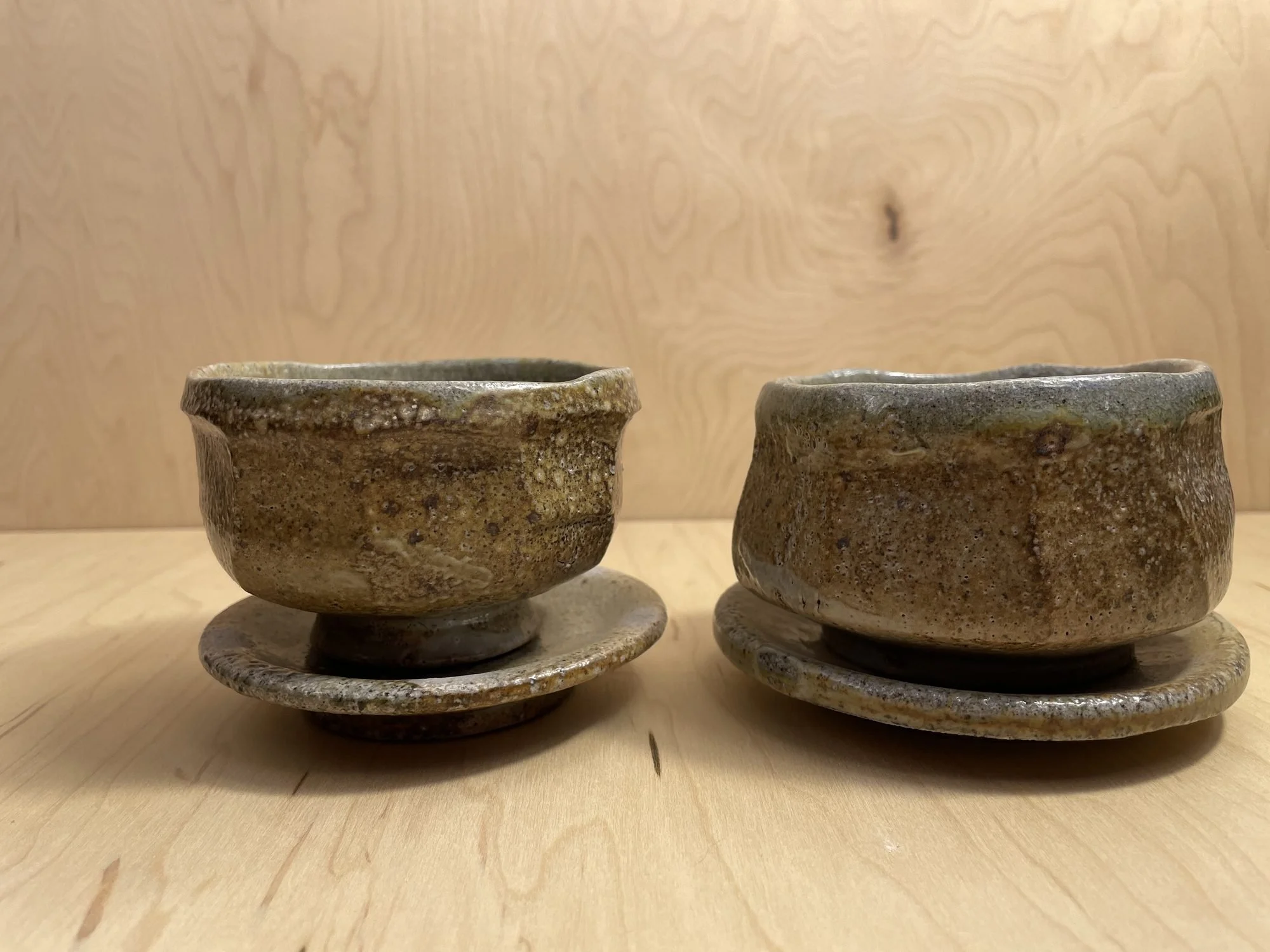 Two cups on matching saucers with a pale grey green surface on a wooden table
