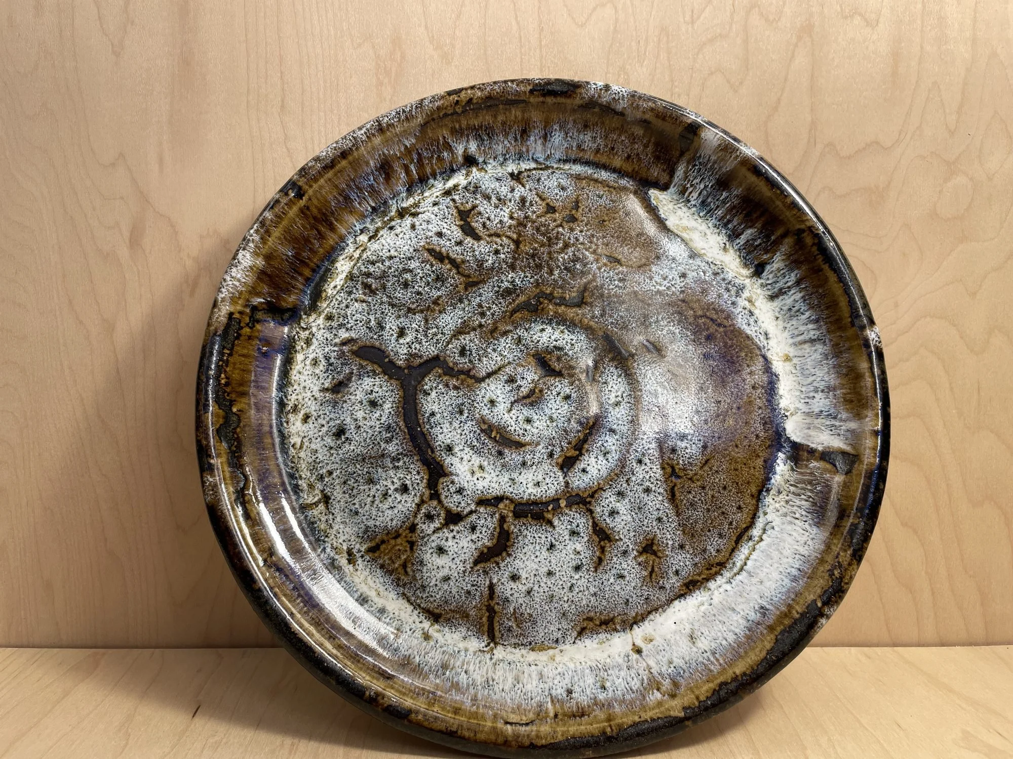 A round glazed stoneware plate with a white spiral and brown speckles standing on a wooden table