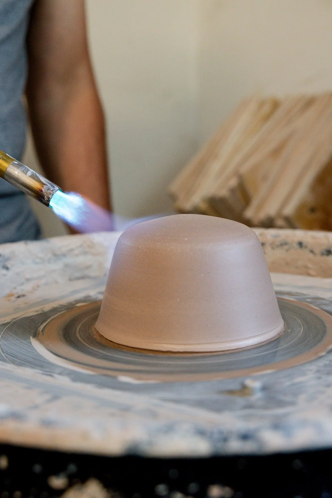 A torch flame drying the outside of an upside down clay bowl on the wheel